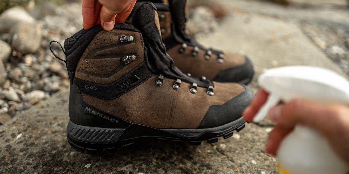 Close-up of a person cleaning Mammut brown and black hiking boots with a spray bottle, ensuring their gear is ready for the next adventure.