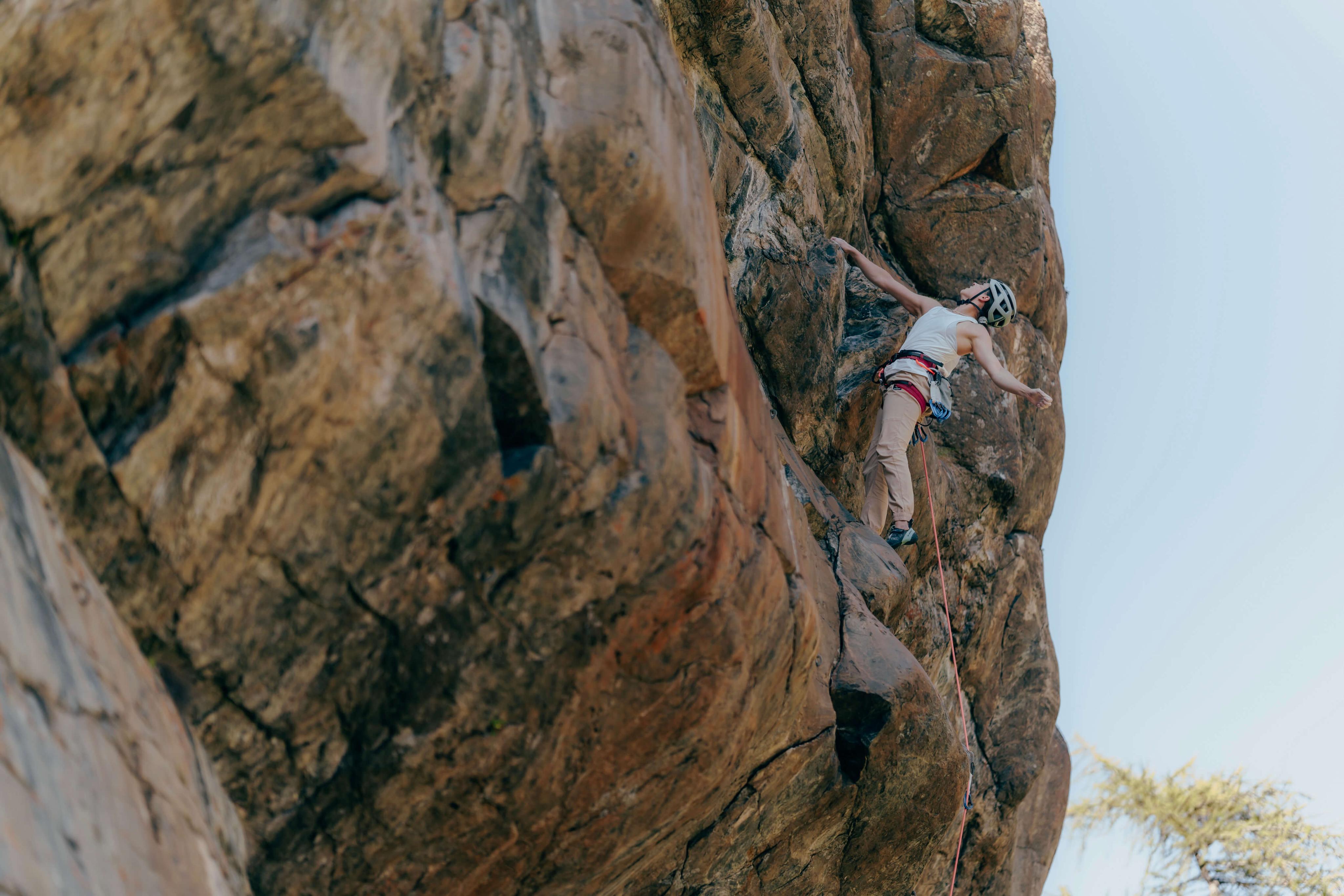 A climber equipped with Mammut climbing gear ascends a challenging rock face under clear, sunny skies.