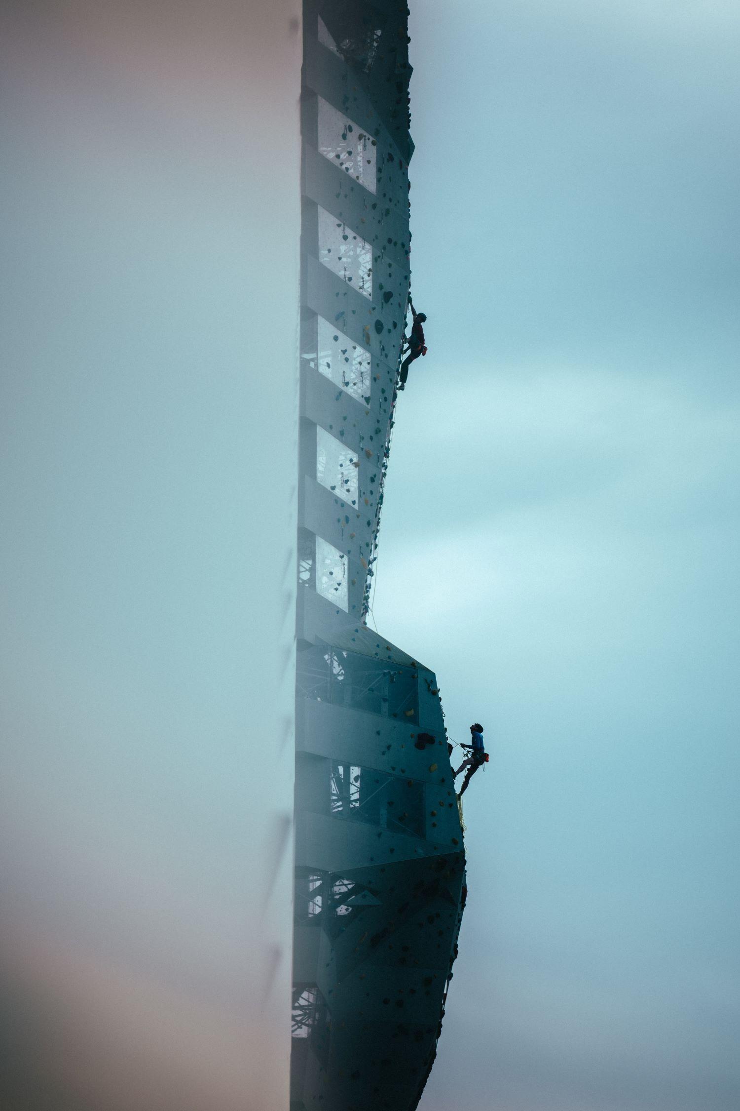 Two climbers scale a towering rock face wearing Mammut gear against a backdrop of a cloudy sky at Copenhill in Denmark.
