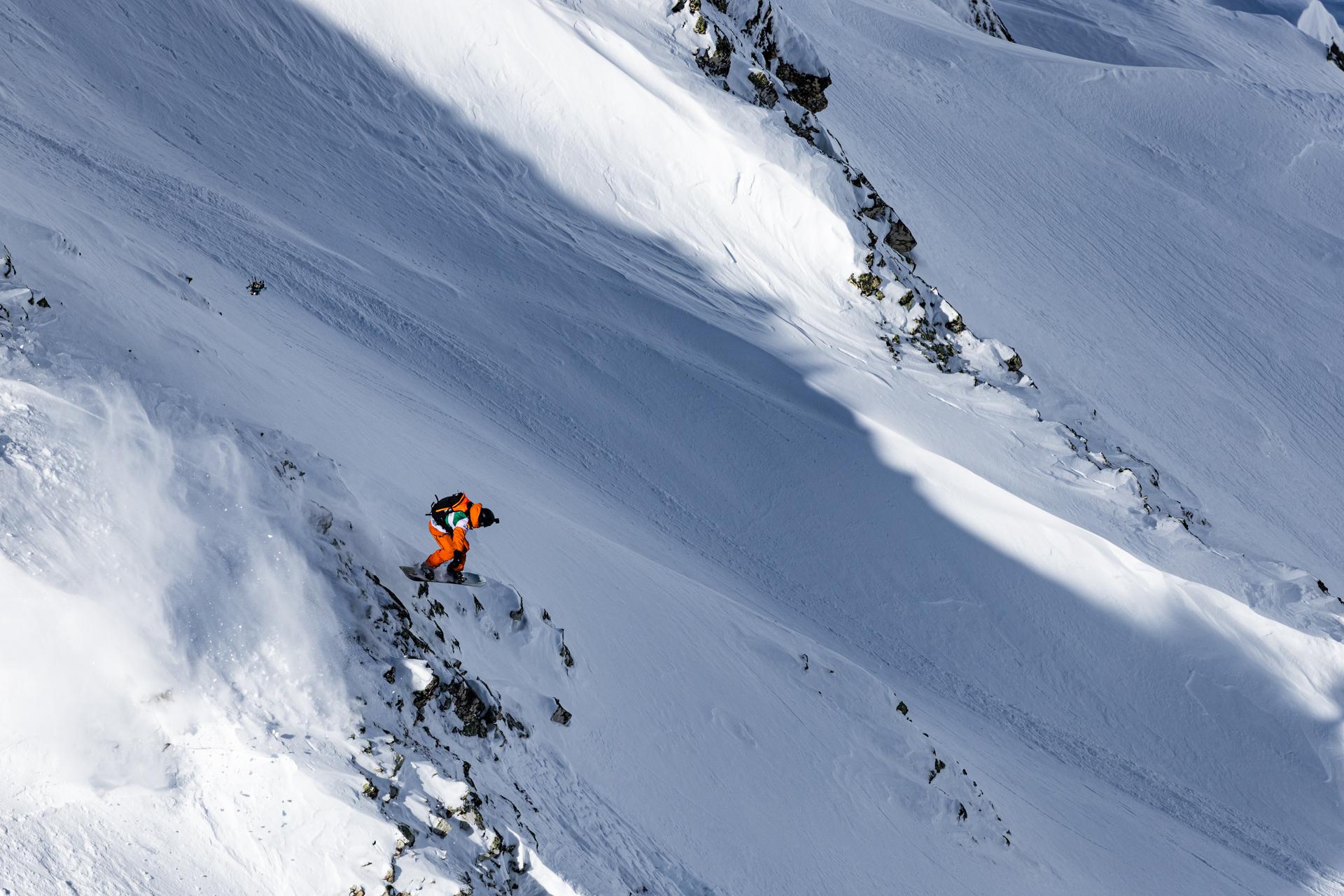 Person wearing a Mammut beanie and insulated jacket looking thoughtful, with sports jerseys blurred in the background.
