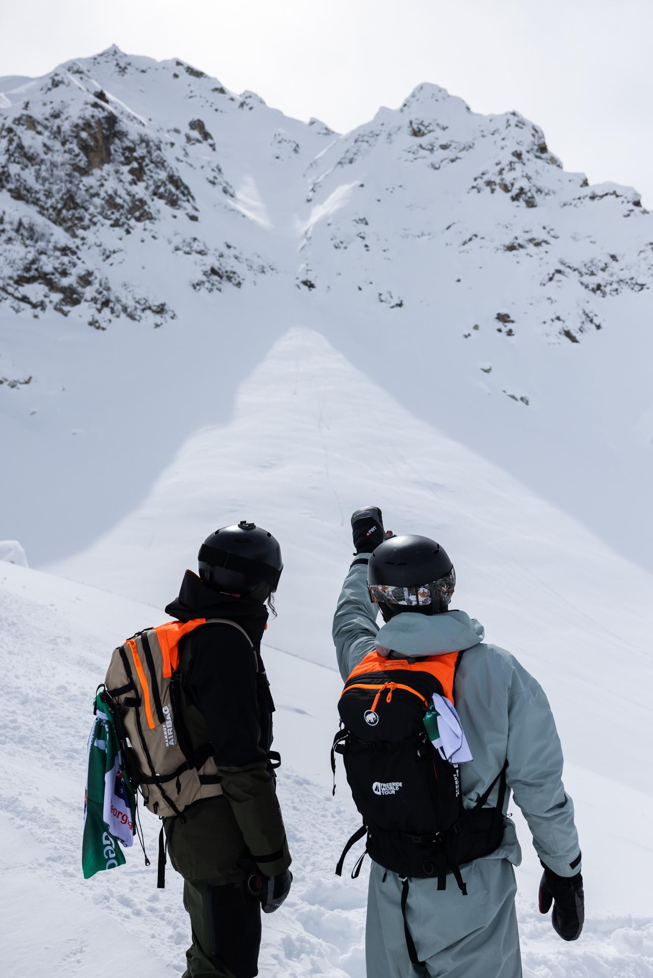 A skier in a beige Mammut outfit and black helmet descends a snowy slope during a race, displaying various sponsor logos.