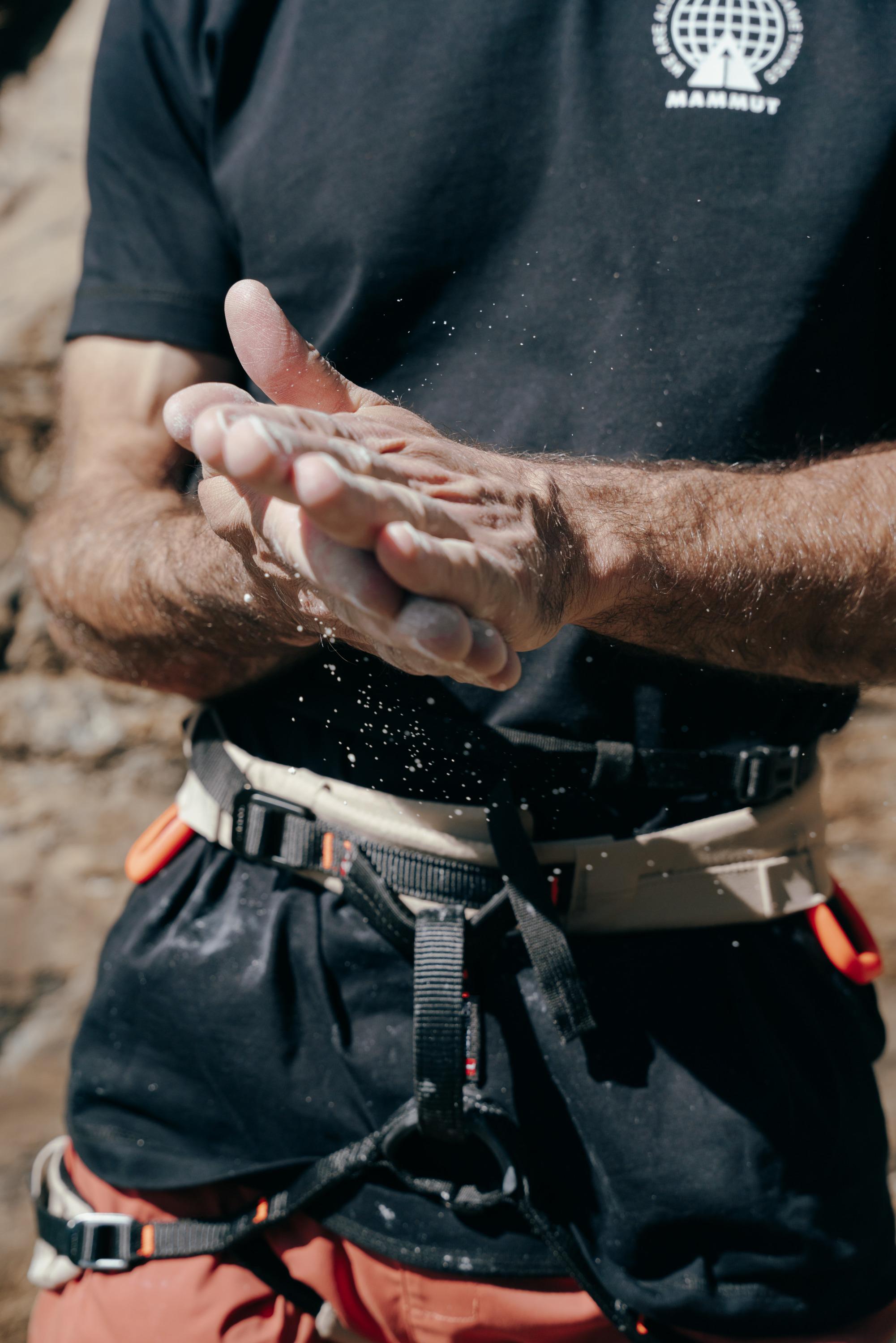 A climber wearing a Mammut harness applies chalk to their hands before ascending.