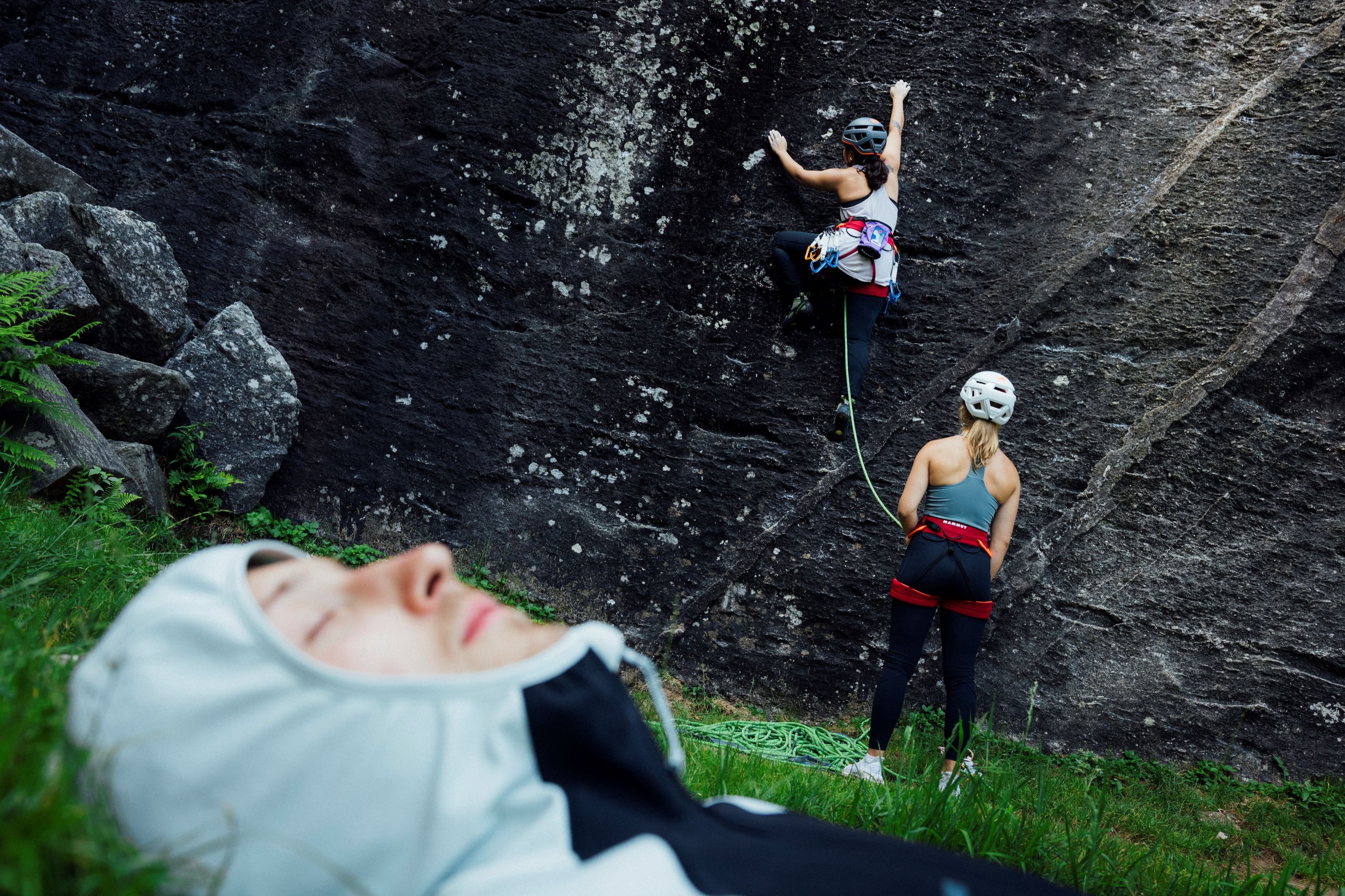 Two rock climbers high-five, smiling with joy, wearing matching vibrant tie-dye outfits from Mammut in a stunning mountainous outdoor setting.