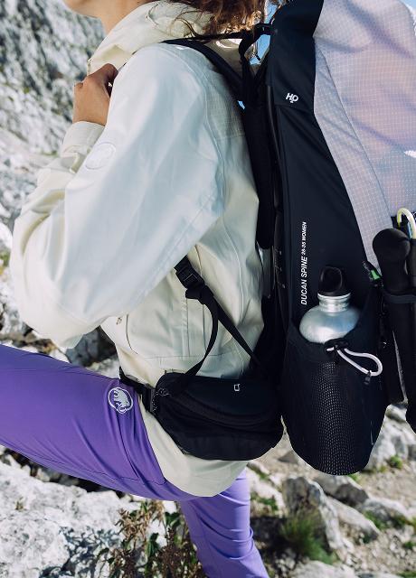 Hiker wearing Mammut backpack and purple pants climbing rocky terrain, with a water bottle in the side pocket.