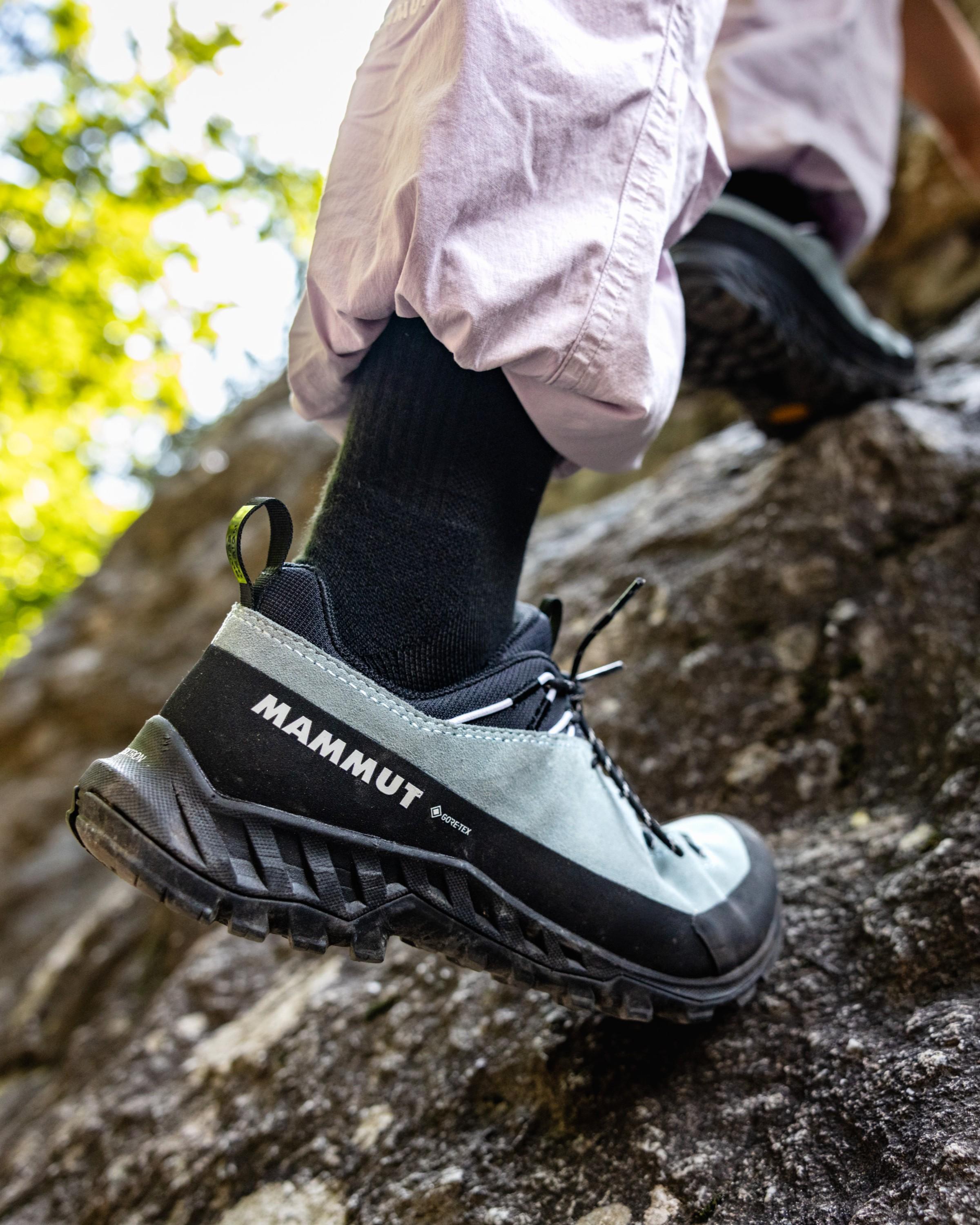 A climber scales an outdoor rock face wearing Mammut hiking shoes and light-colored pants, showcasing Mammut mountaineering gear.