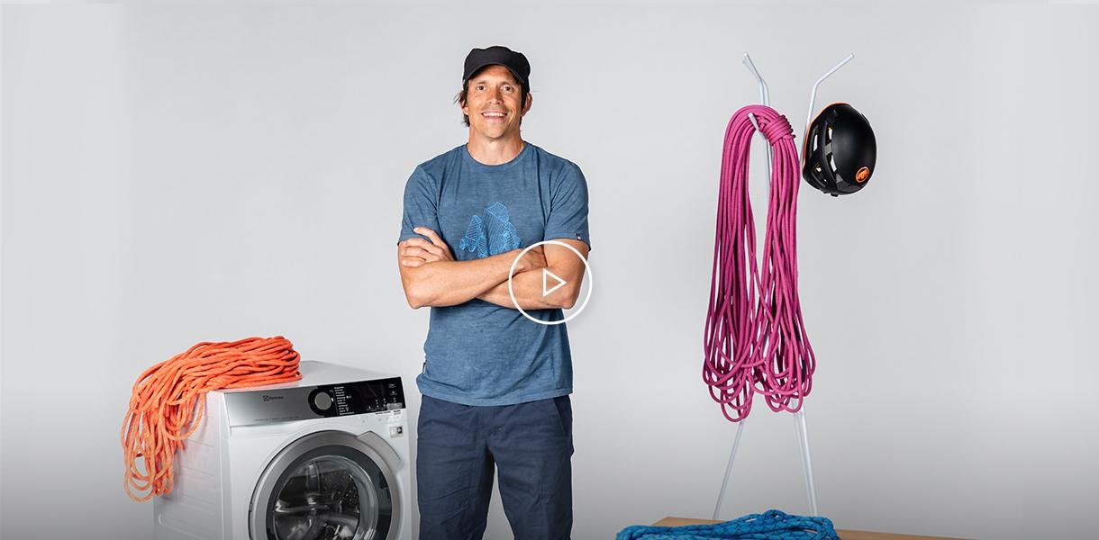 A man stands beside a washing machine with Mammut mountain climbing gear, including ropes and a helmet.