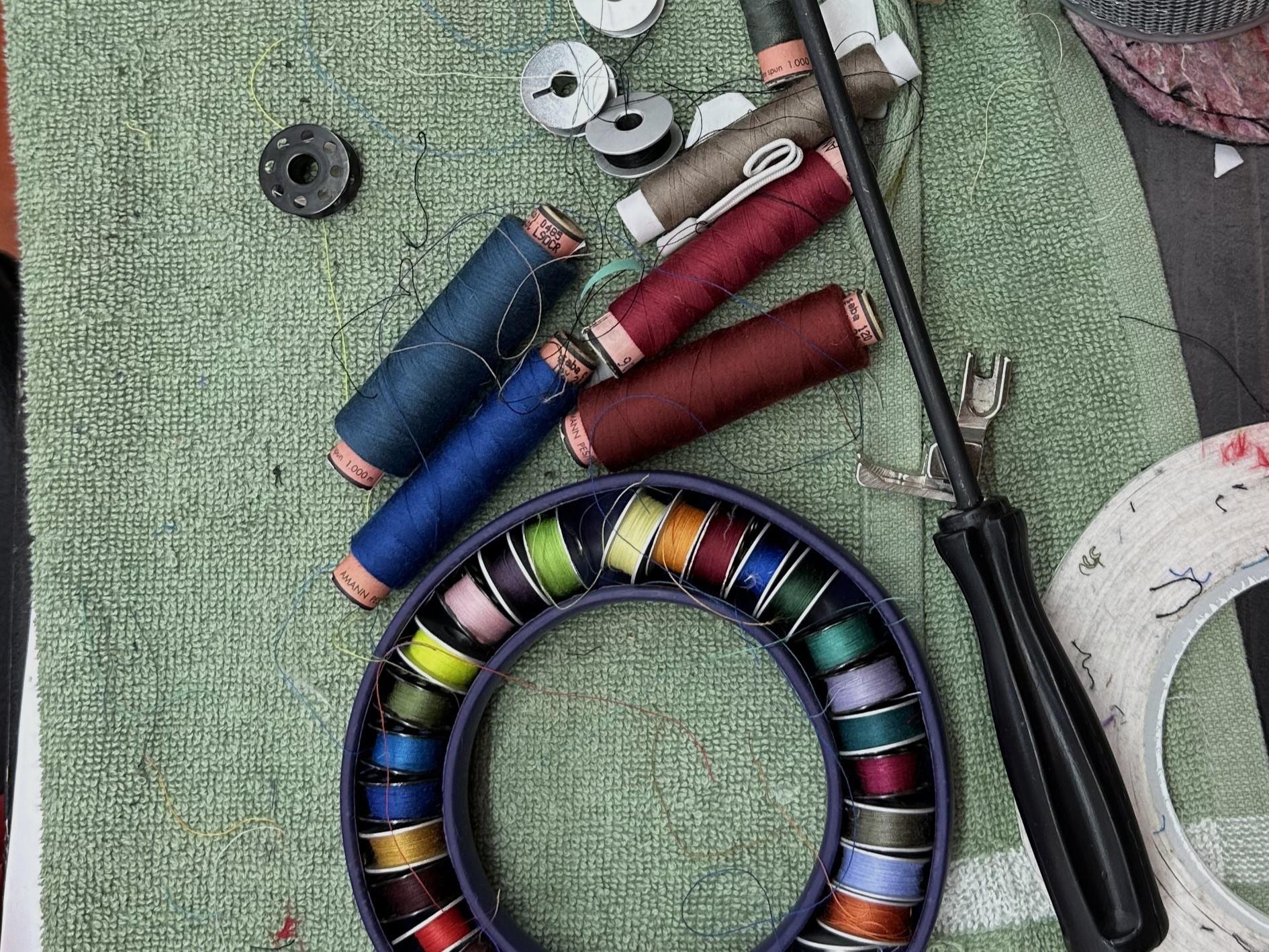 A sewing kit with vibrant thread spools, bobbins, and essential tools neatly arranged on a green fabric surface, perfect for repairing or customizing Mammut outdoor gear.