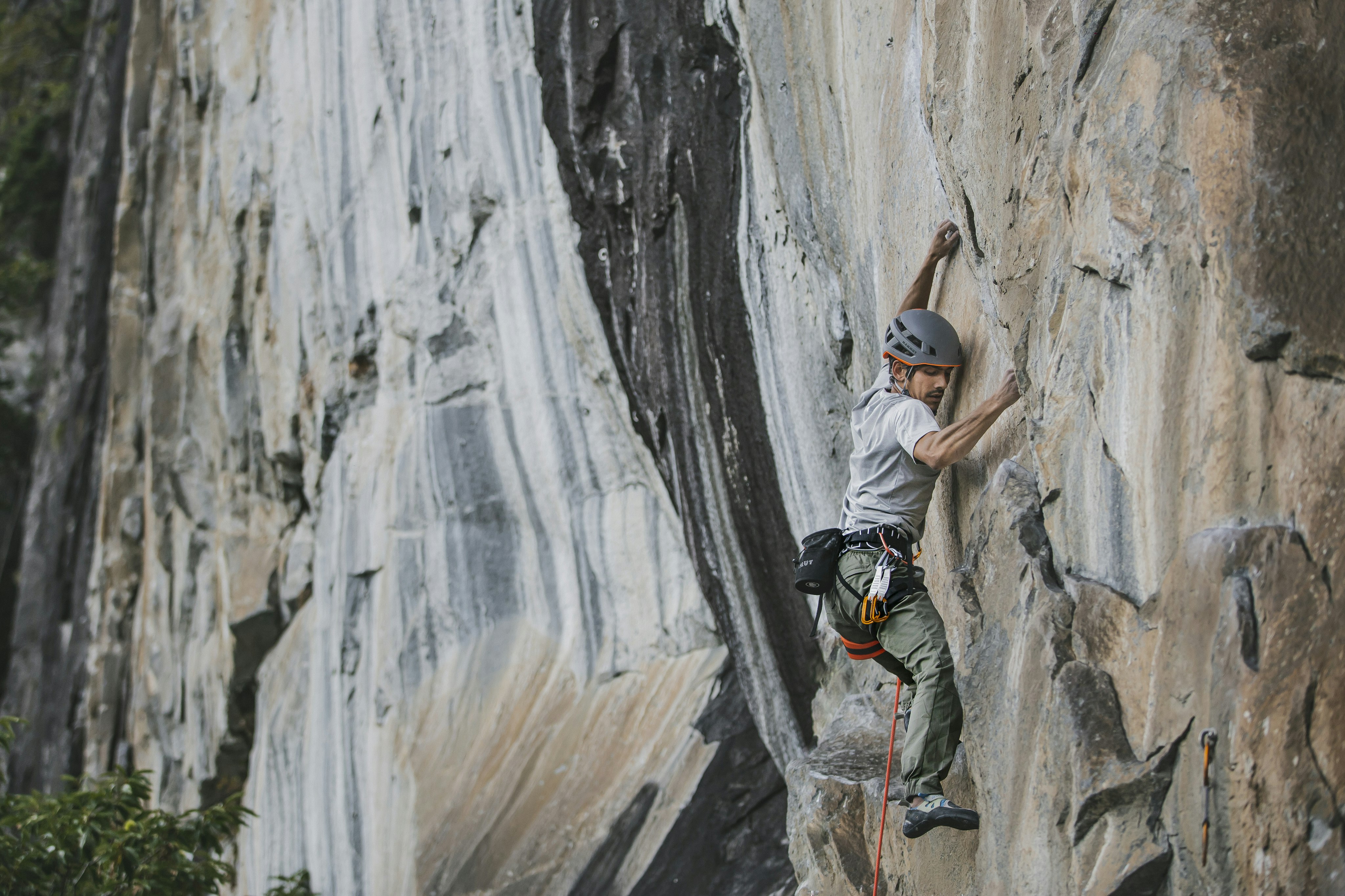 Mann klettert an einer hohen Felswand mit Mammut Kletteroutfit