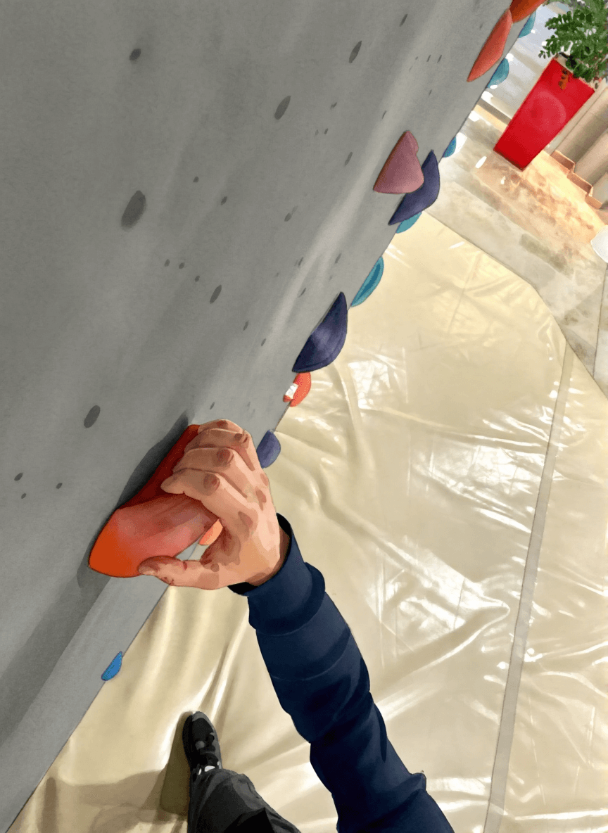 A woman rock climbing indoors, wearing Mammut gear, grips a large handhold labeled "JUG" as another climber ascends in the background.