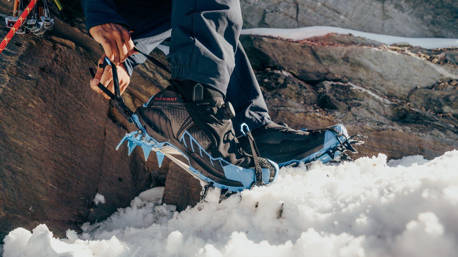 A climber in Mammut blue gear and helmet organizes climbing rope on a snowy alpine mountain under a clear blue sky.