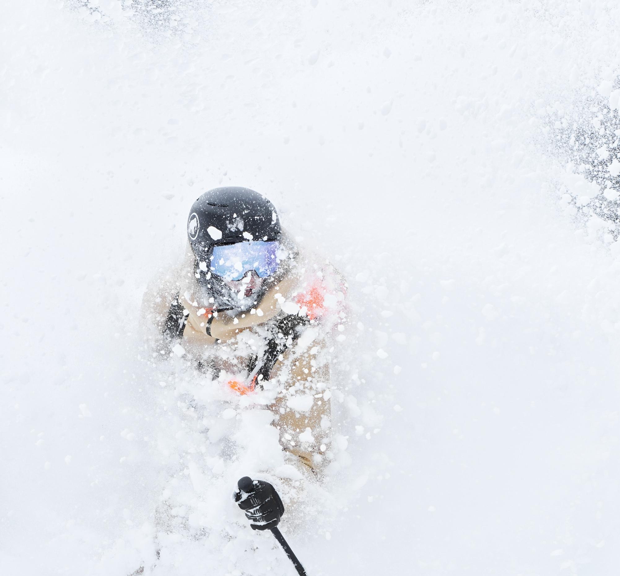 Skier wearing a Mammut helmet and goggles, carving through a spray of snow, capturing an exhilarating, wintry scene.
