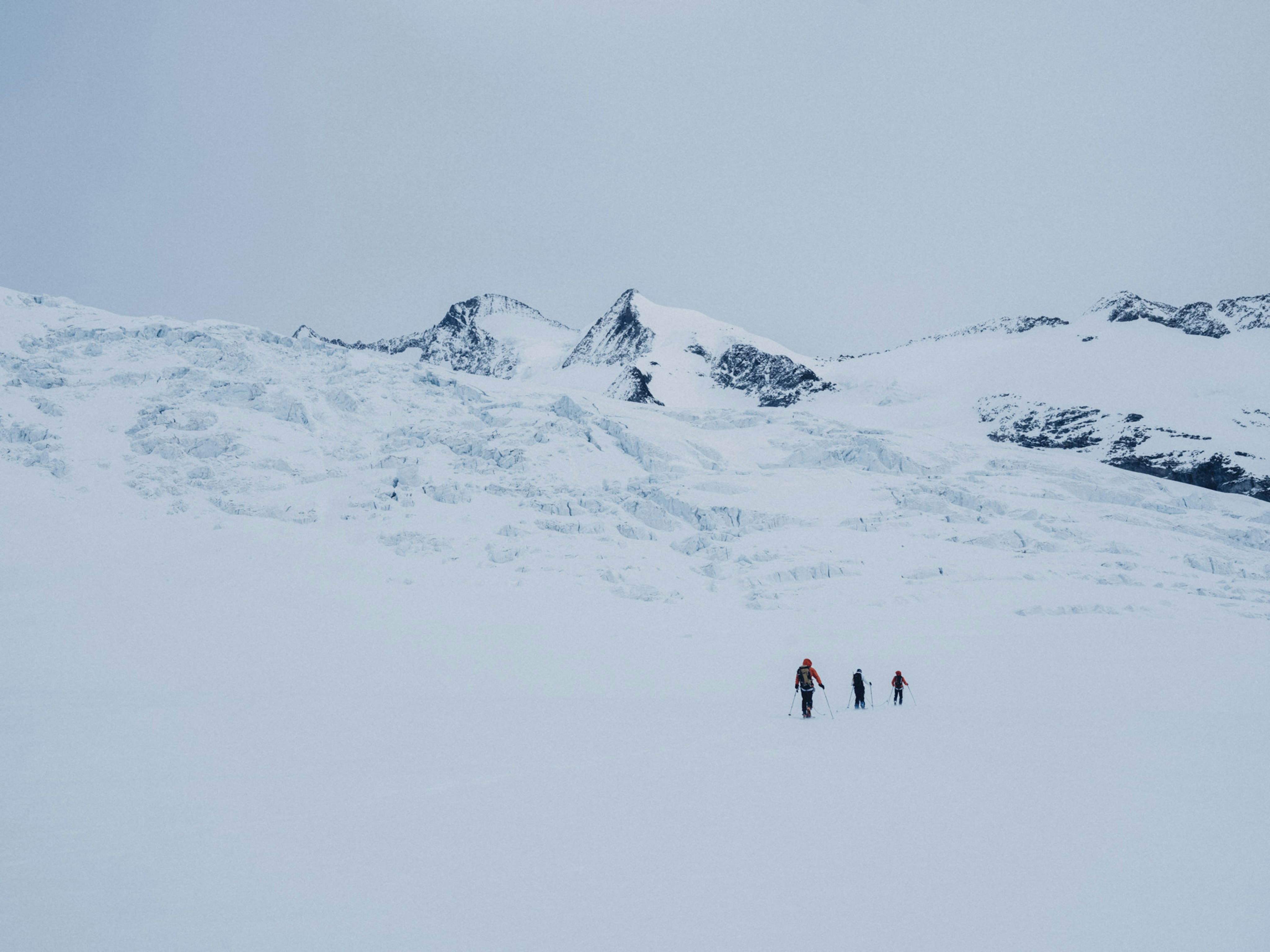 Three people walking in the snow on a glacier.