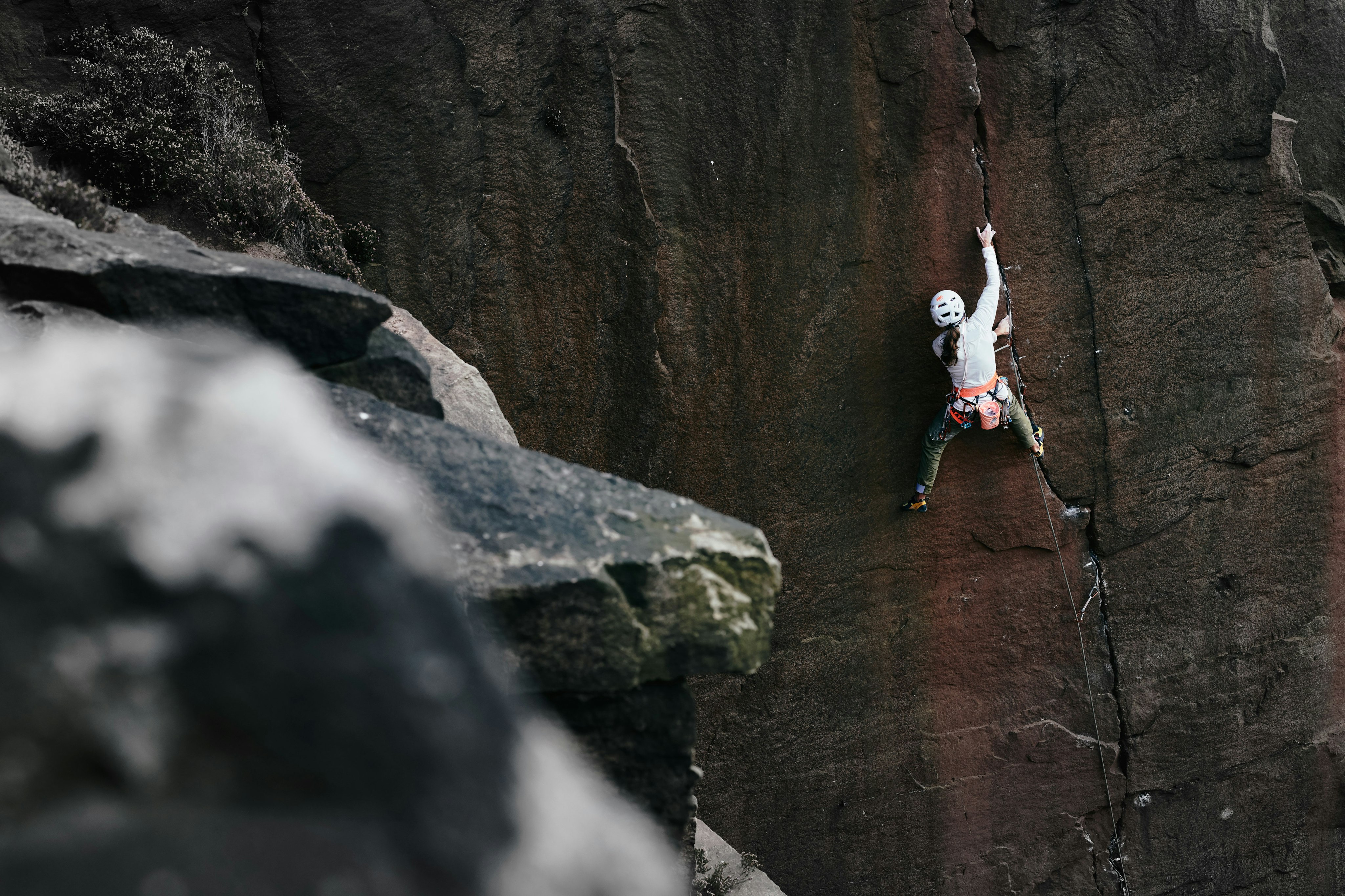 Woman climbing secured on dark rock wall in Mammut outfit