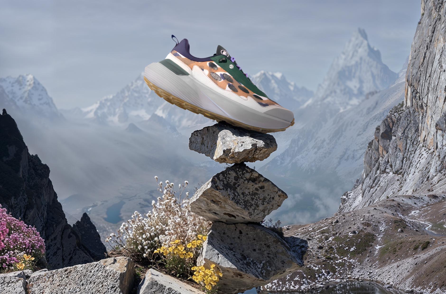 A colorful Mammut sneaker balanced on stacked rocks in an alpine mountain landscape, featuring wildflowers and snowy peaks.