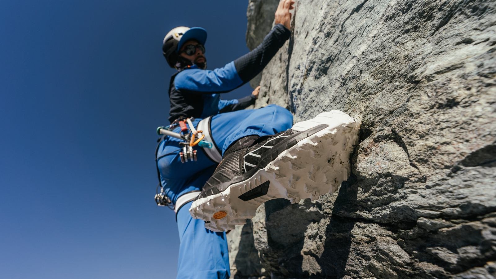 A skier in yellow Mammut gear carves downhill through fresh powder snow, leaving a dynamic trail behind.