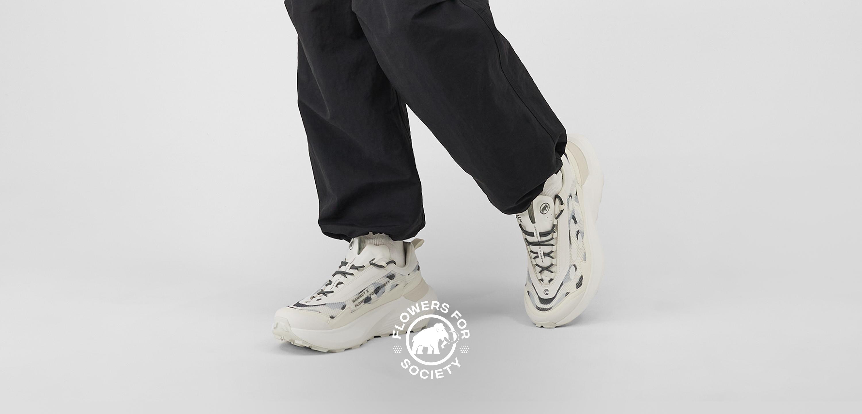 Person wearing white chunky Mammut sneakers and black pants, with "Flowers for Society" logo displayed beneath their feet.