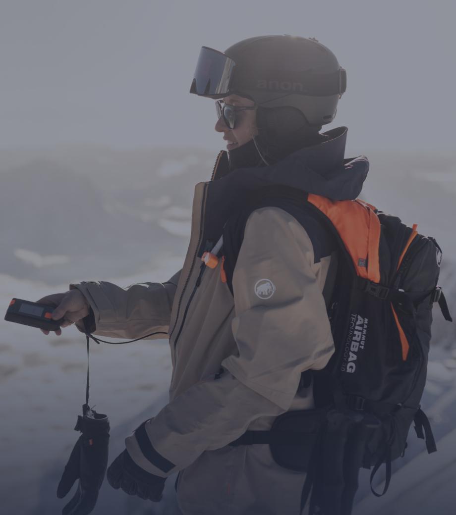 Skier in Mammut gear with backpack and helmet navigating a snowy mountain terrain using an avalanche safety device.
