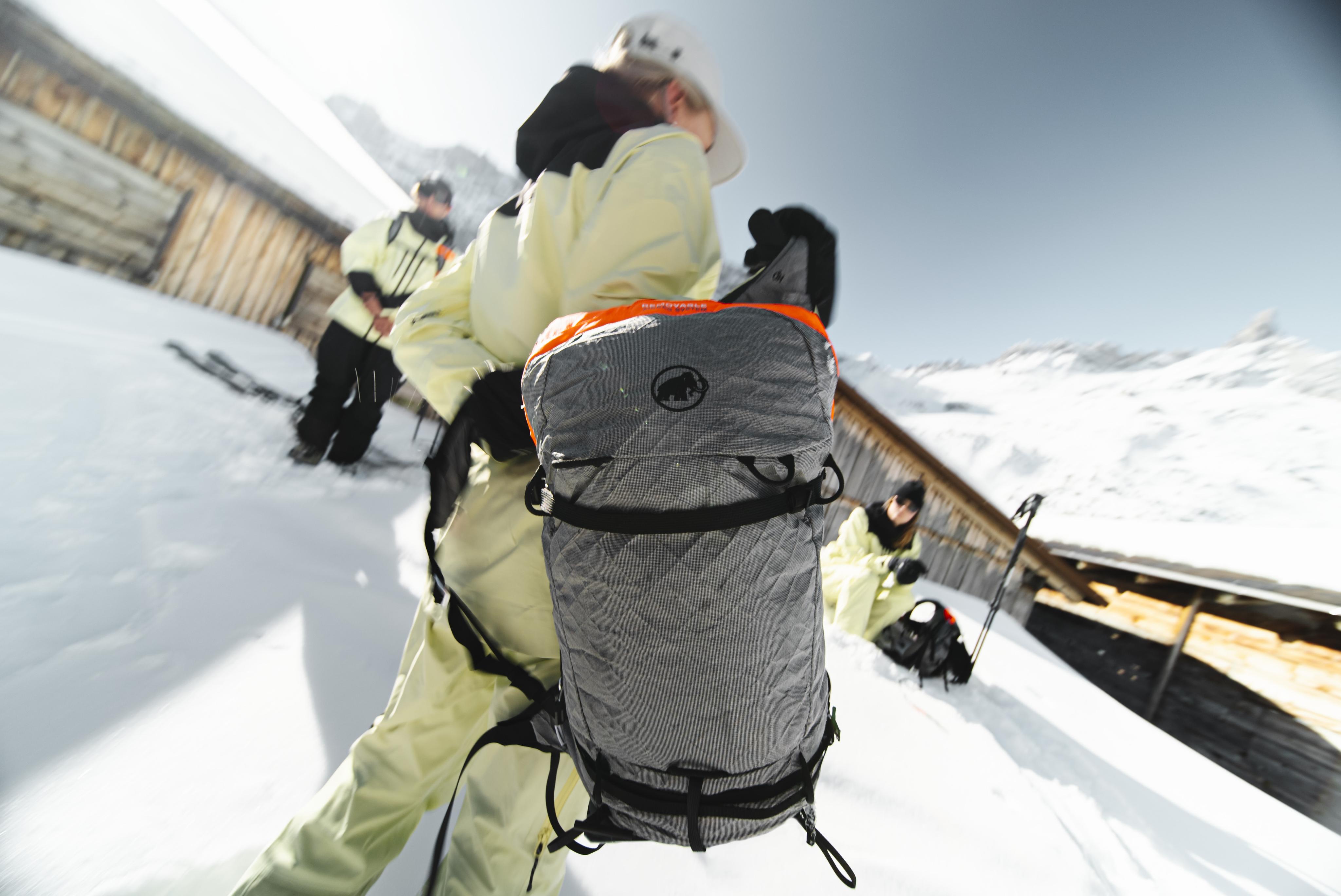 Skier in Mammut gear with backpack and helmet navigating a snowy mountain terrain using an avalanche safety device.