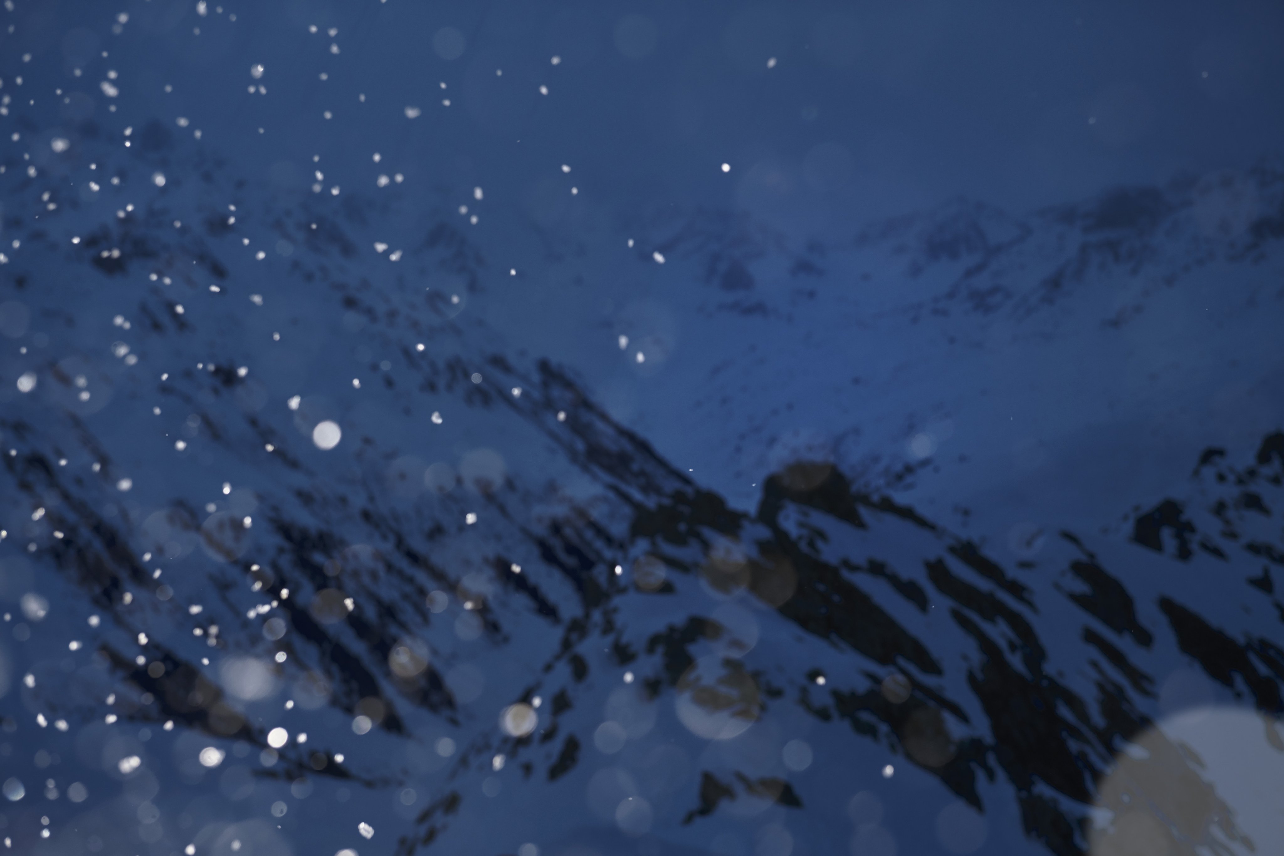 Snow falling in front of snow-covered mountains under a dark, overcast sky at dusk, embodying the adventurous spirit of Mammut mountaineering.