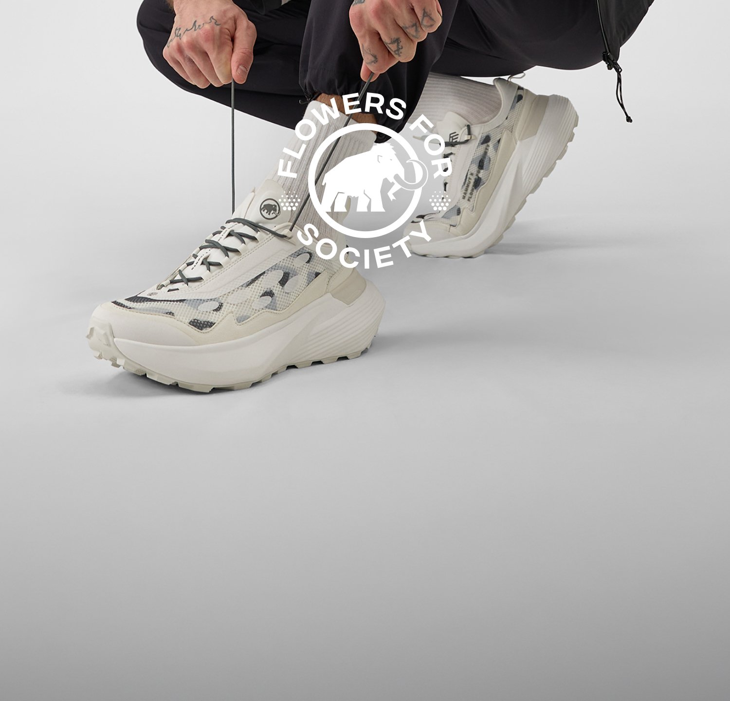 Person wearing white and gray chunky Mammut sneakers with black pants; "Flowers for Society" logo over the image.