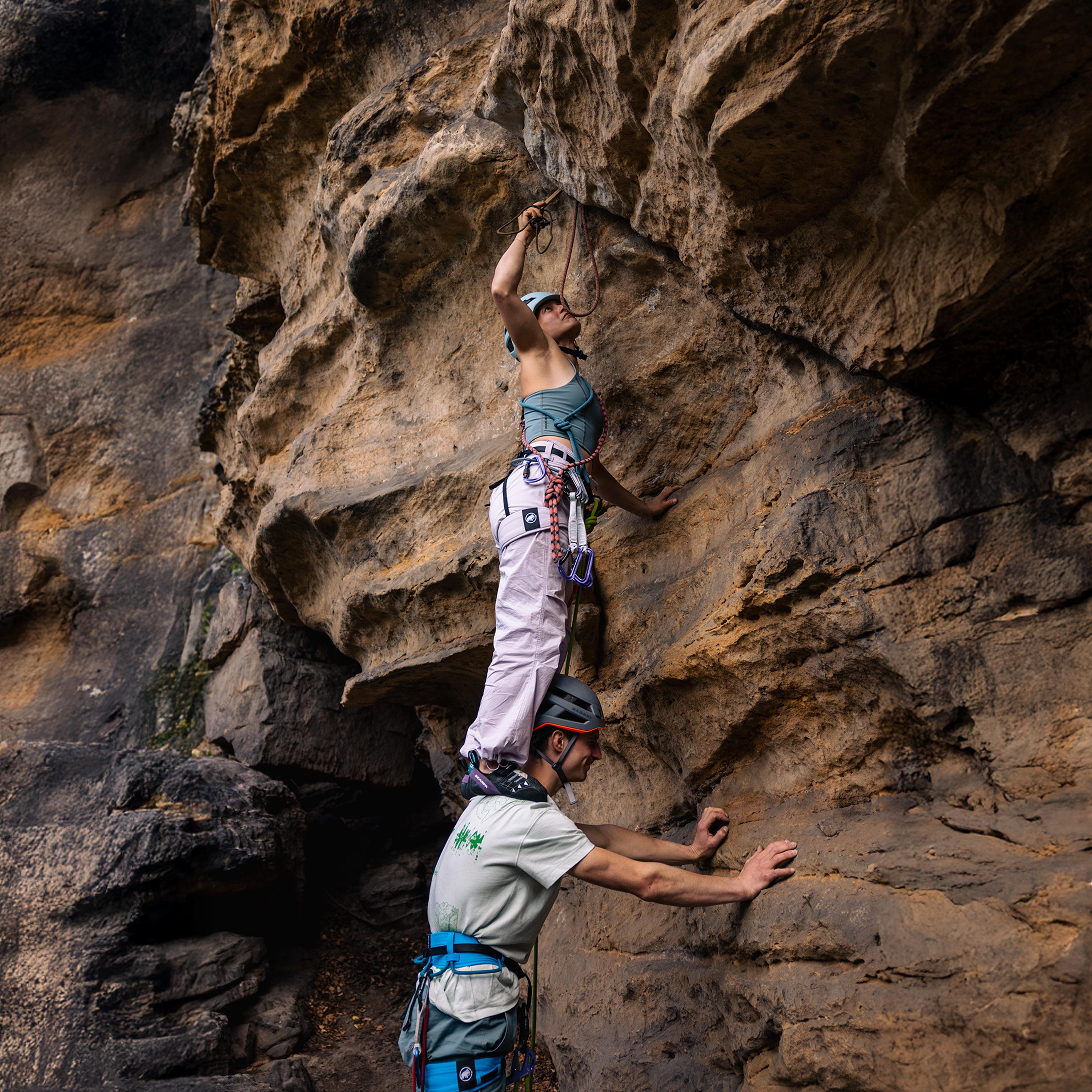 Climber in a helmet scaling a steep, dark cliff using Mammut climbing gear and rope, showcasing advanced mountaineering skills.