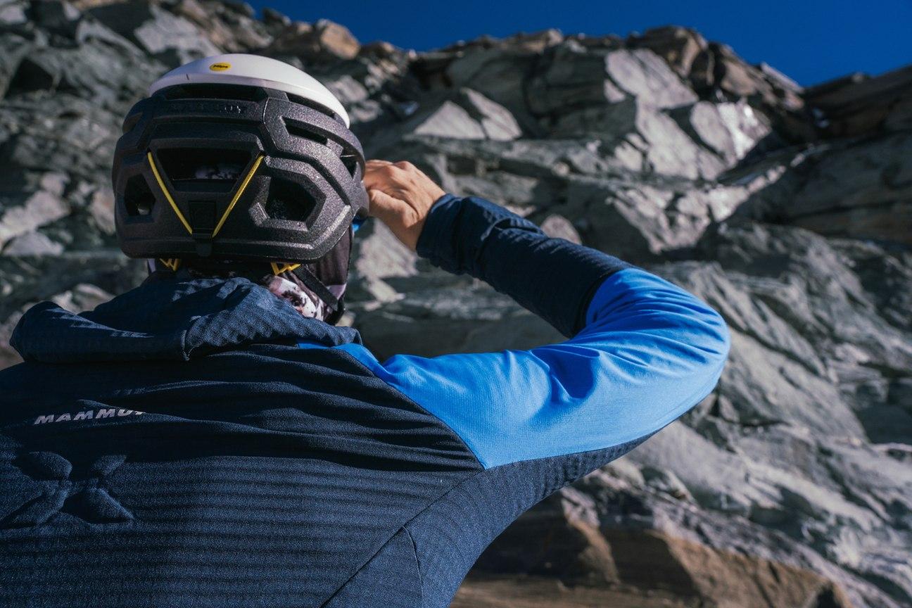 Two climbers wearing helmets and Mammut mountaineering gear organize equipment on a snowy, foggy mountainside.
