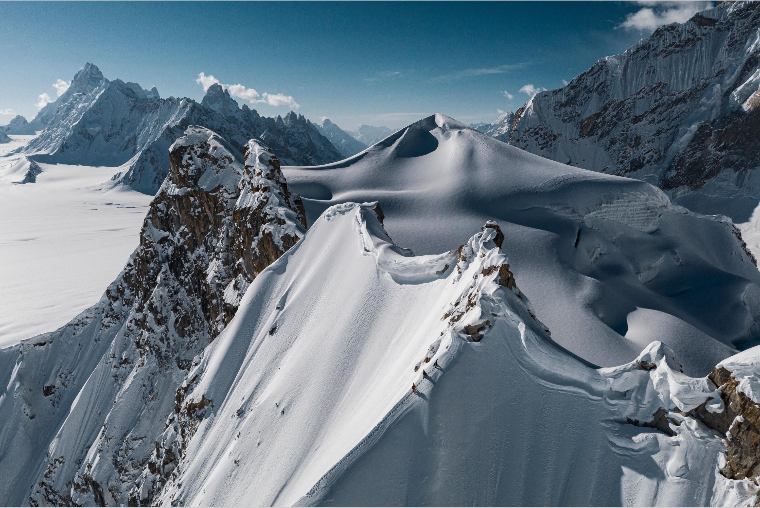 Snow-covered mountain peaks under a clear blue sky, featuring jagged ridges and a vast snowy expanse, ideal for Mammut mountaineering gear.