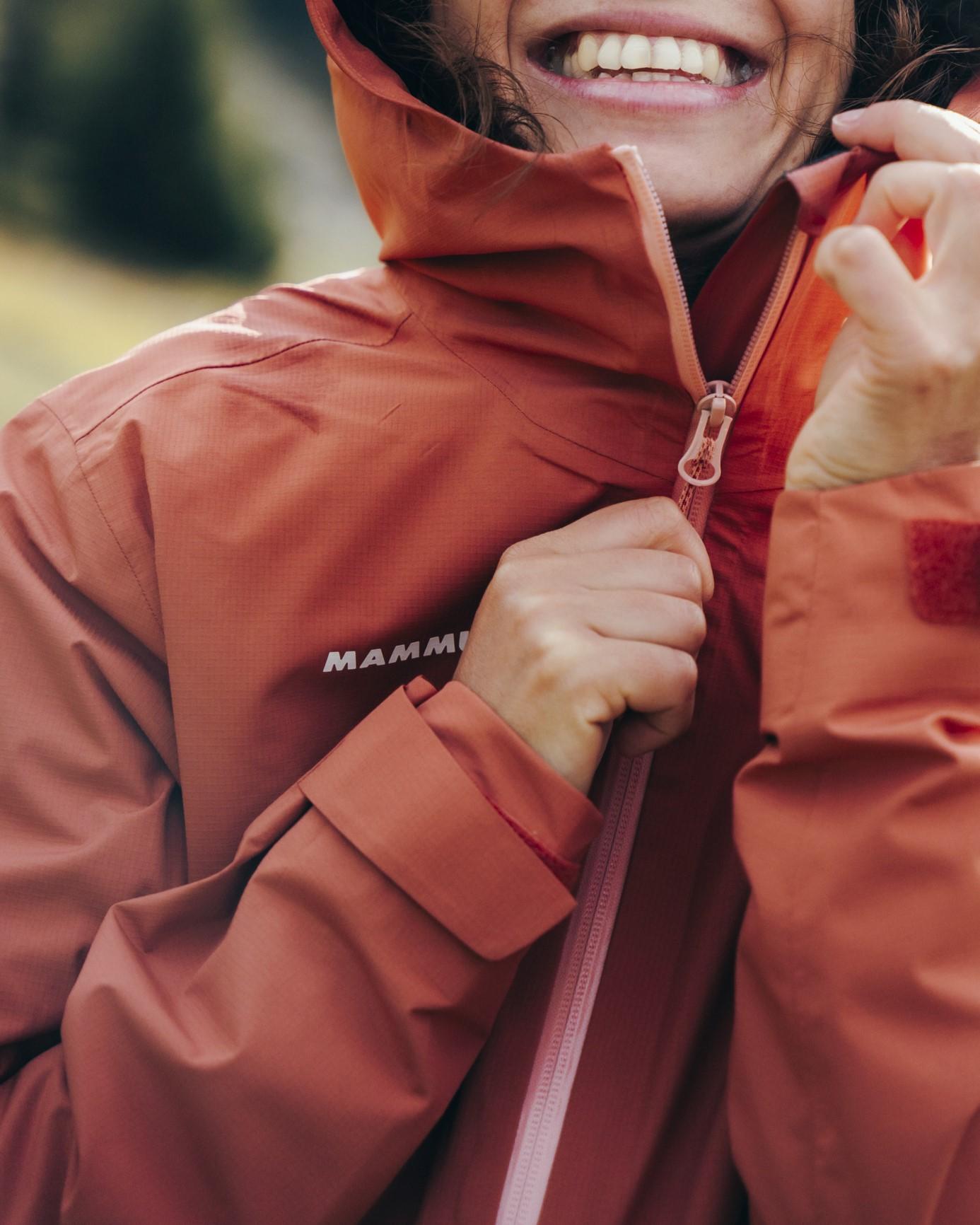 Person smiling while zipping up an orange Mammut outdoor jacket.