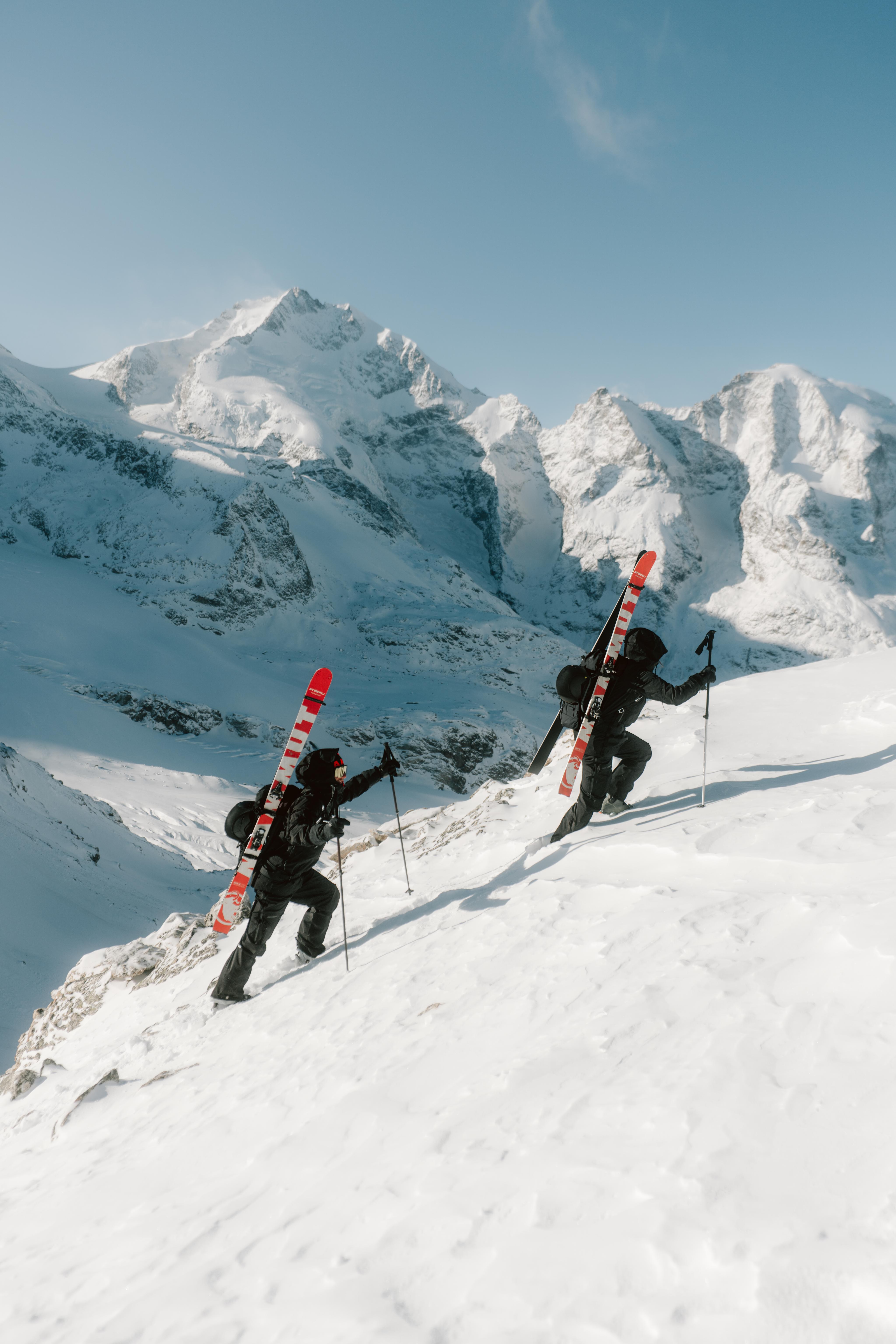 Person in Mammut winter gear and helmet stands in snowy alpine mountains against a bright blue sky.