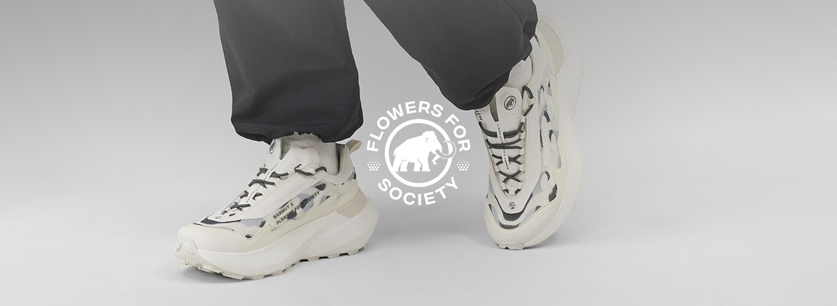Person wearing chunky Mammut white sneakers and black athletic pants, with "Flowers for Society" logo displayed near their feet.