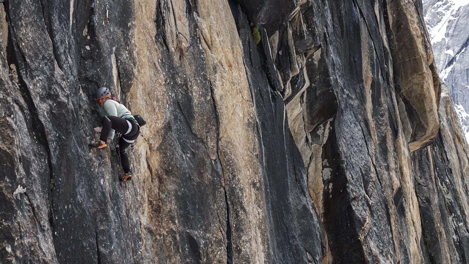Person rock climbing a steep, rugged cliff face wearing Mammut safety gear and helmet.