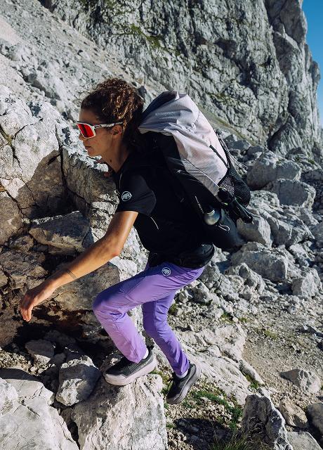 Mammut athlete climbing rocky terrain with a Mammut backpack, wearing purple pants and red sunglasses on a sunny day.