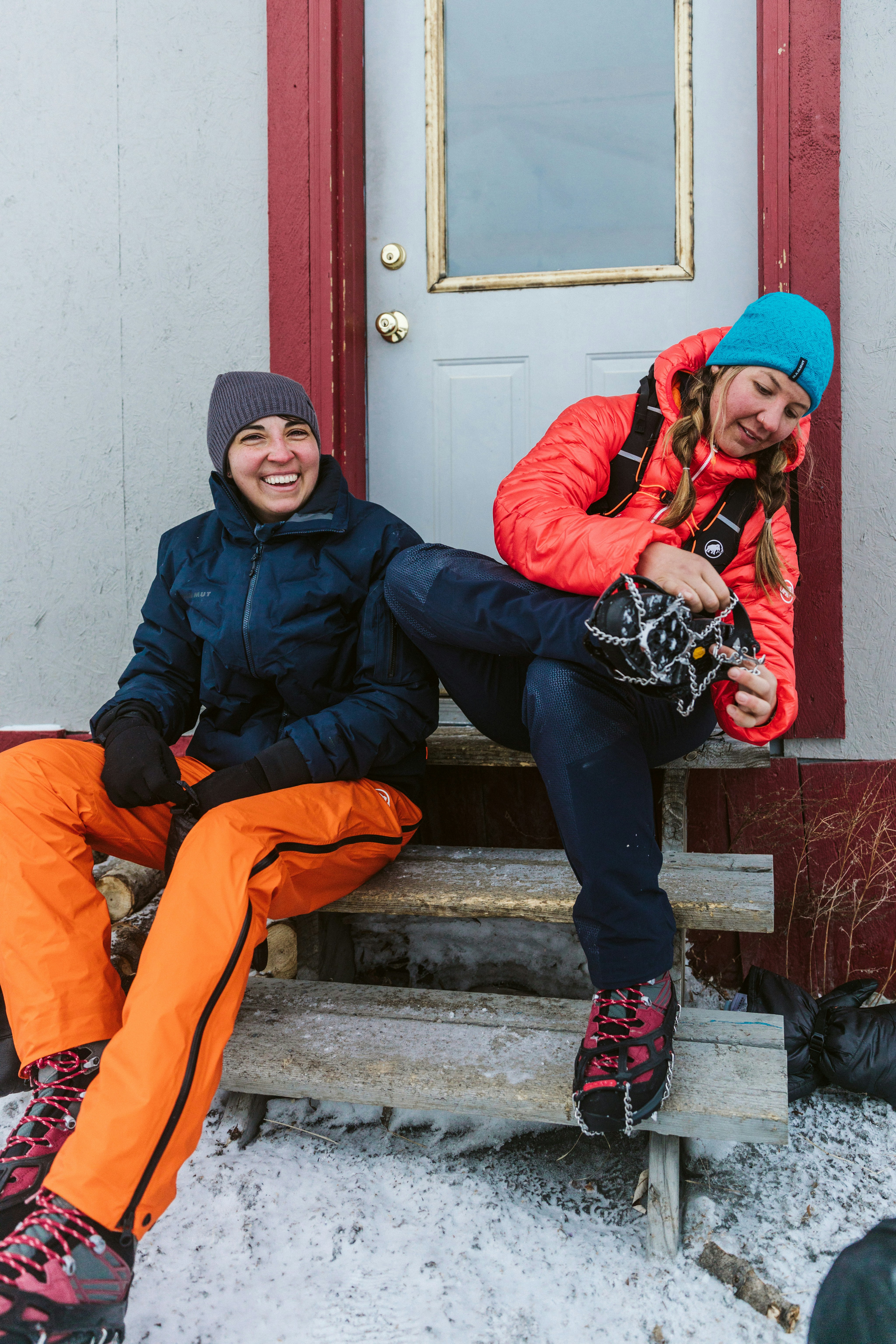 Two people sitting in front of a hut wearing Mammut clothing