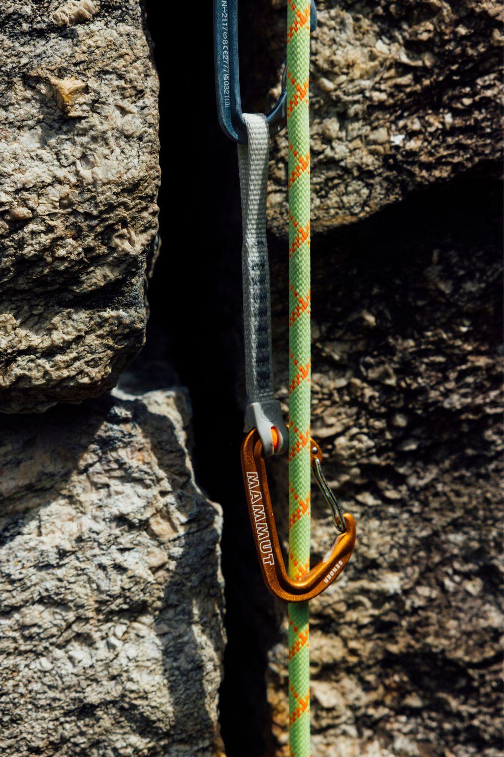 A Mammut climbing quickdraw and rope securely attached to a rock wall during a sport climbing ascent.