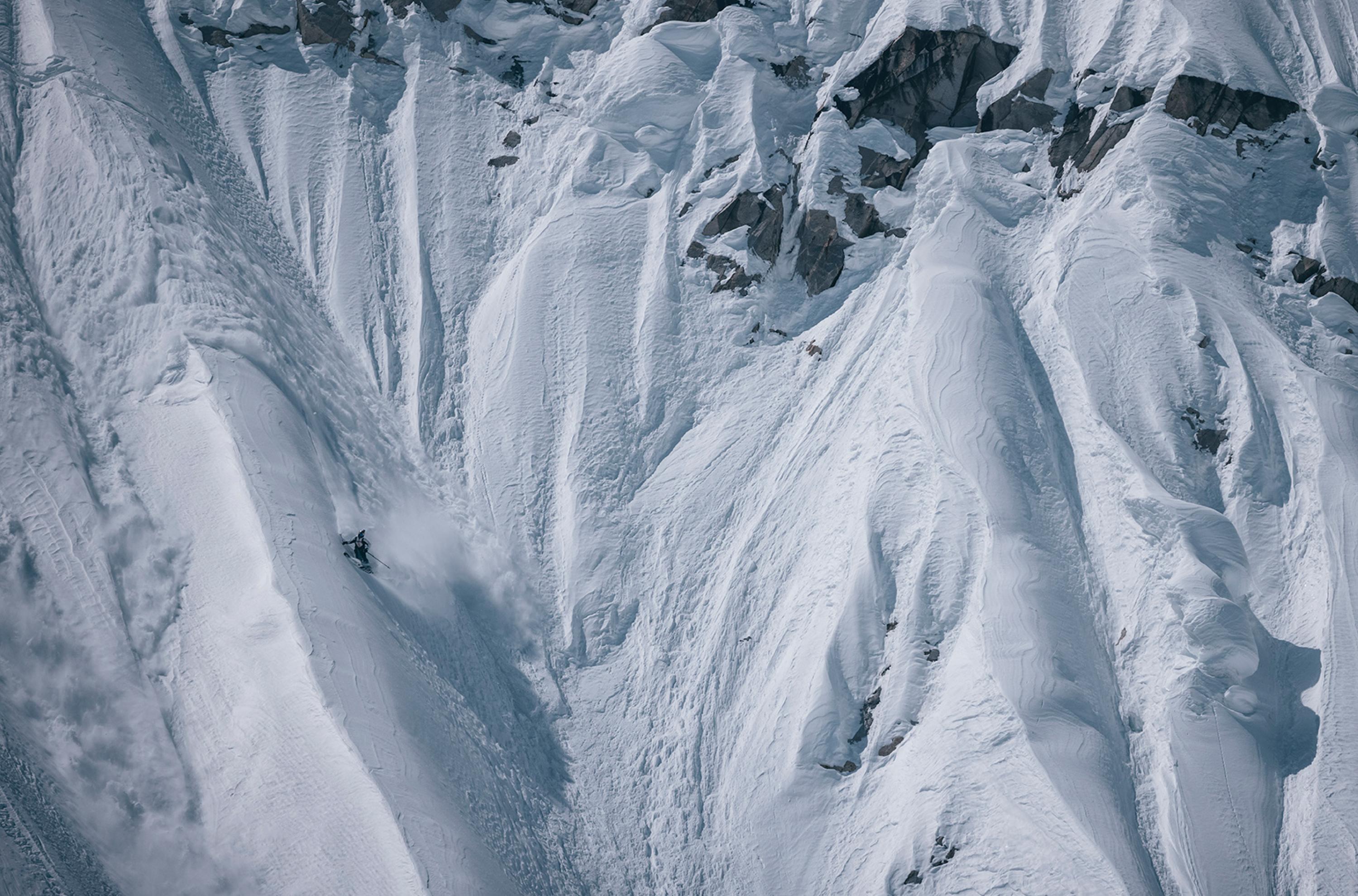 Steep, snow-covered mountain face with jagged rocks and narrow crevices, showcasing a rugged and icy landscape ideal for Mammut mountaineering gear.