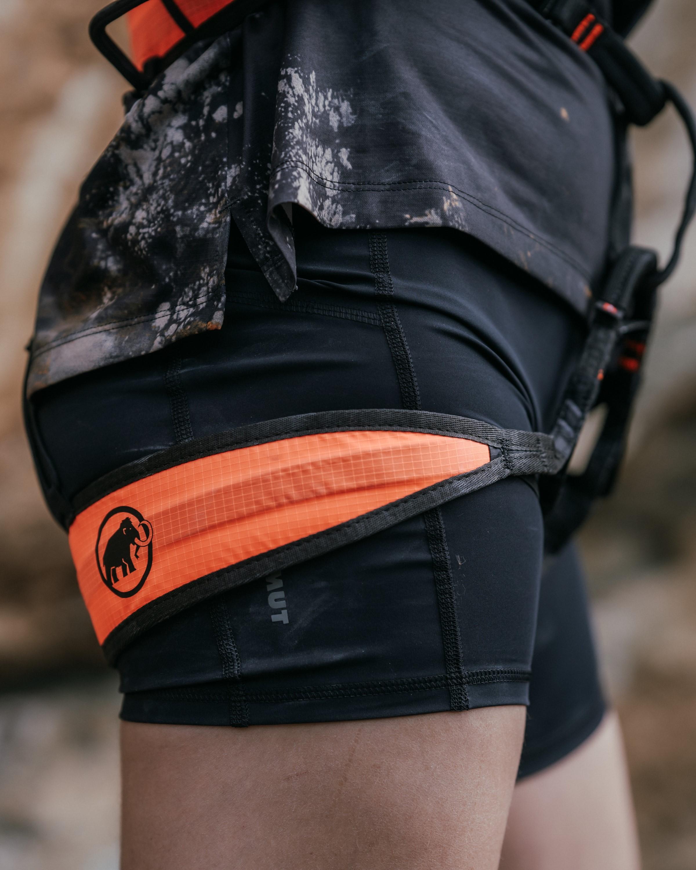 Close-up of a climber wearing a Mammut black and orange climbing harness, featuring the mammoth logo prominently on the orange section.