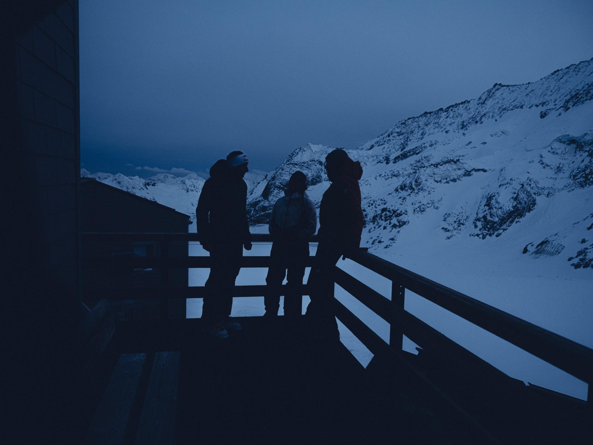 Three people standing on a veranda in the mountains.