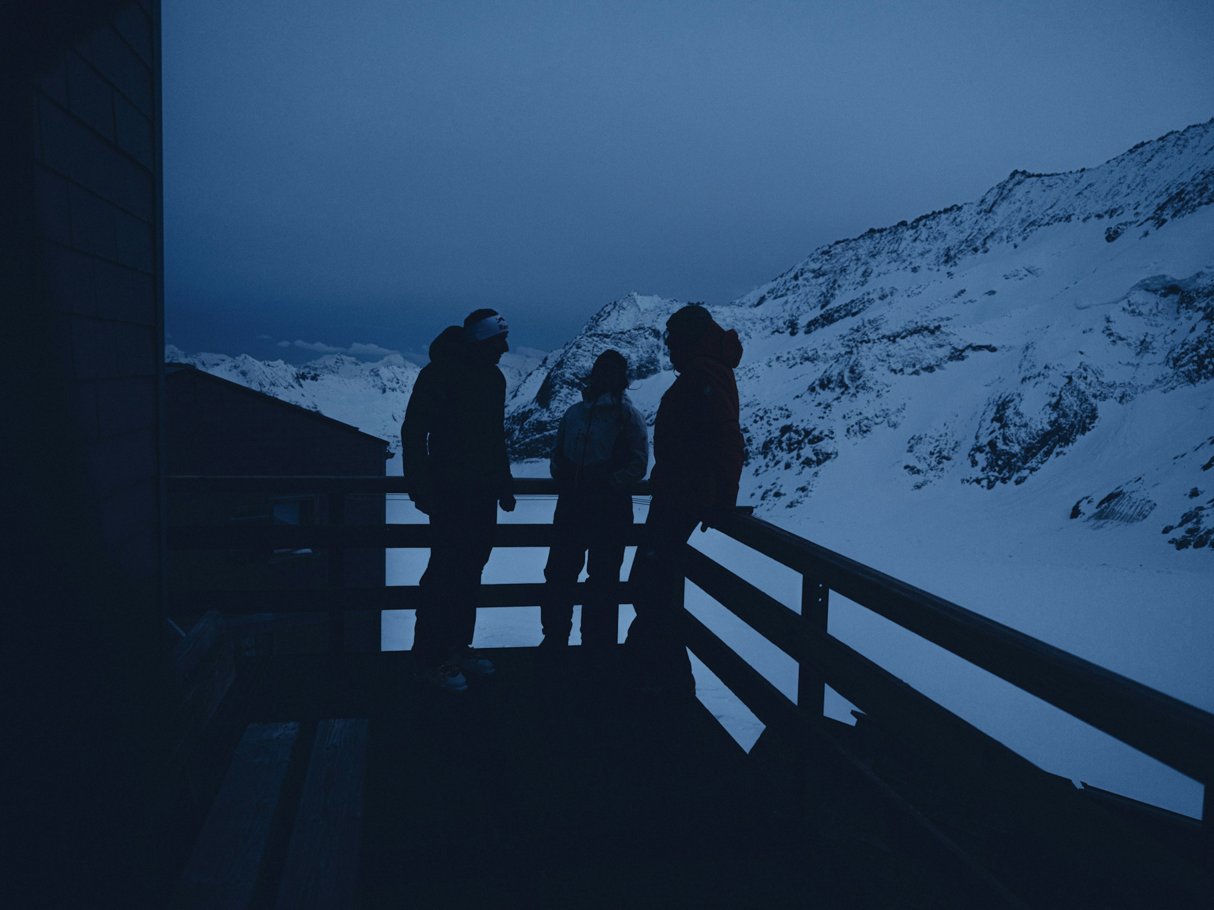 Drei Personen stehen auf einer Veranda in den Bergen. 