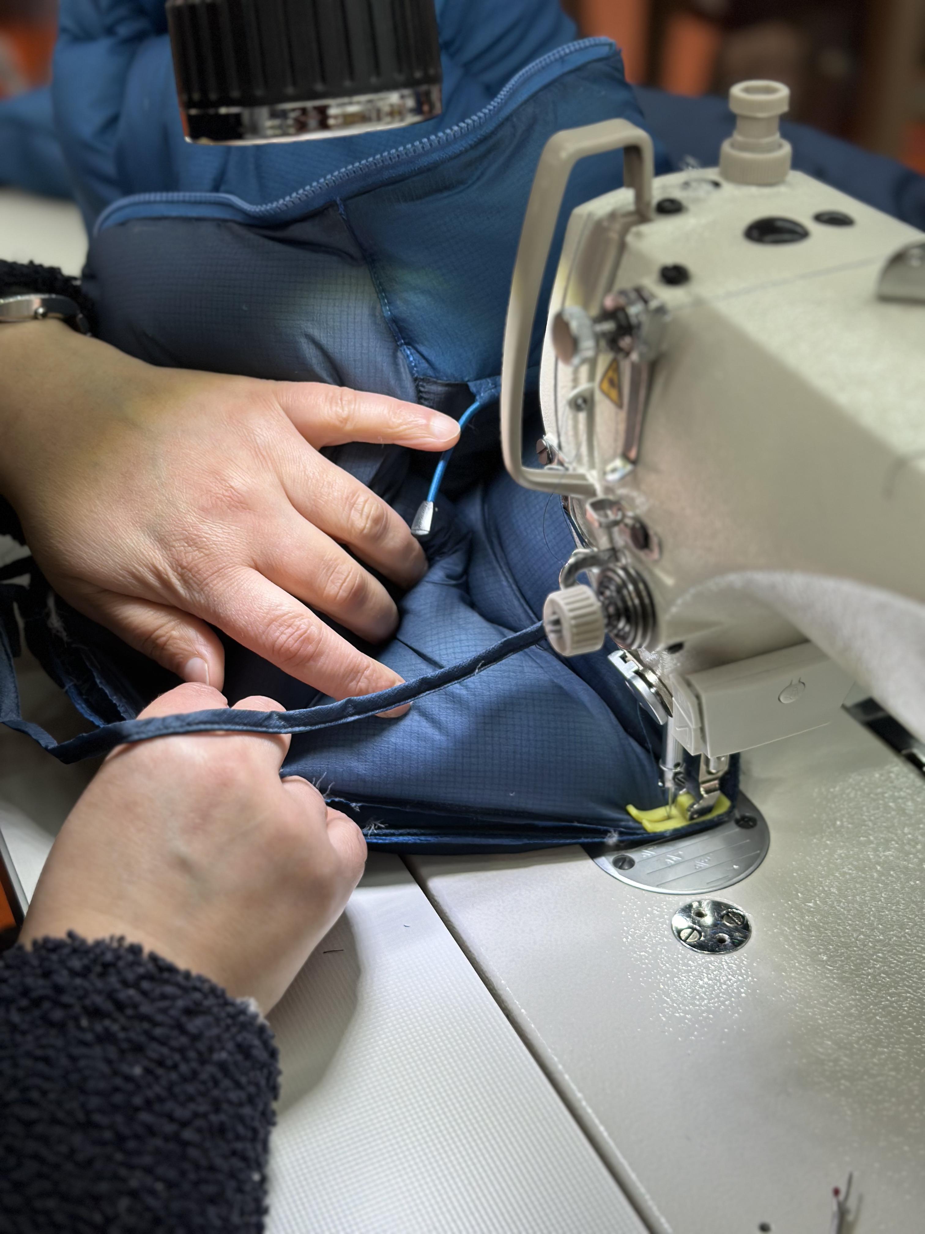 Close-up of hands operating a sewing machine, meticulously stitching blue fabric for Mammut outdoor gear.