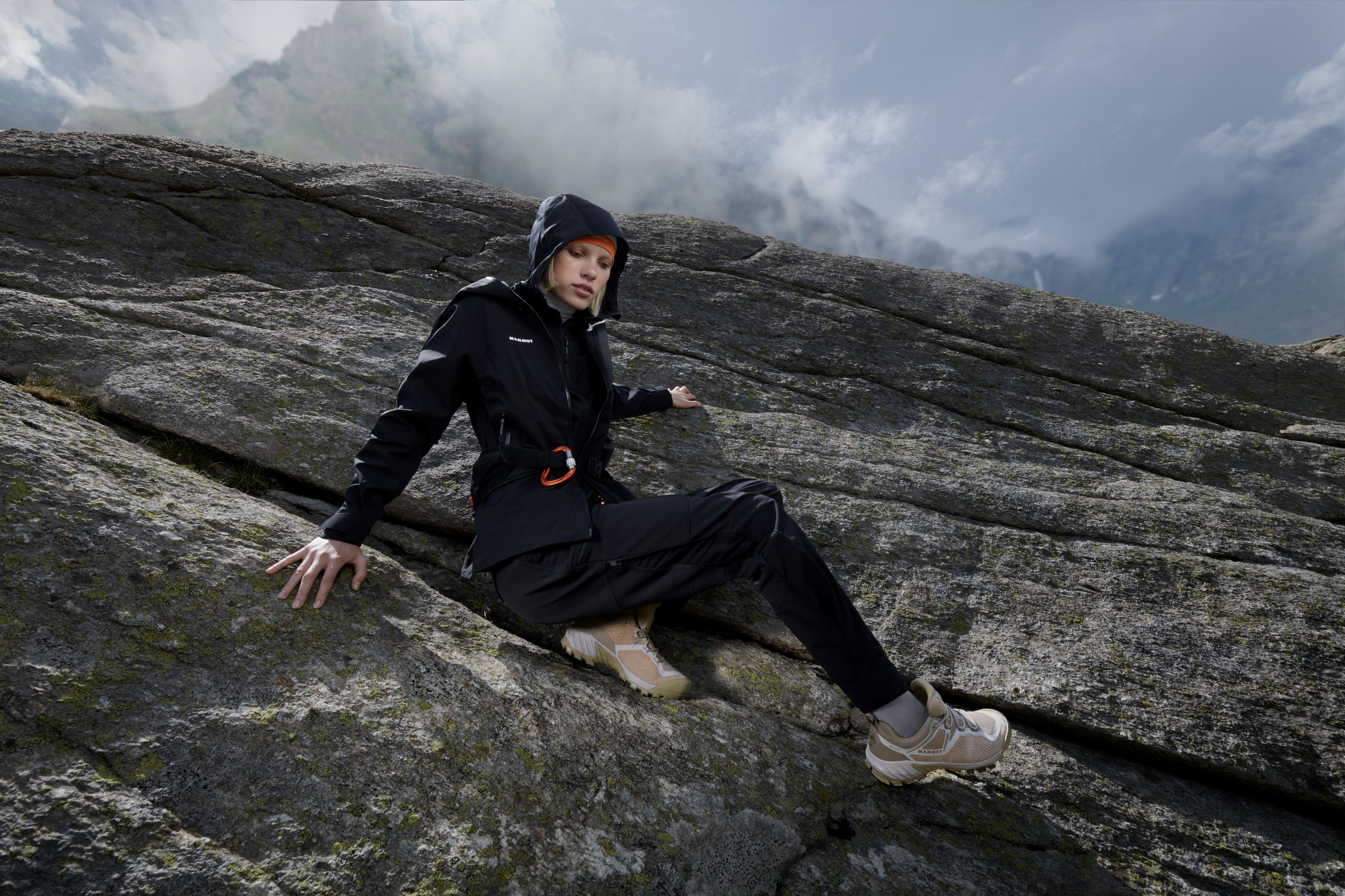 Person wearing Mammut hiking gear and sneakers, sitting on a large rock, with a misty mountain background.