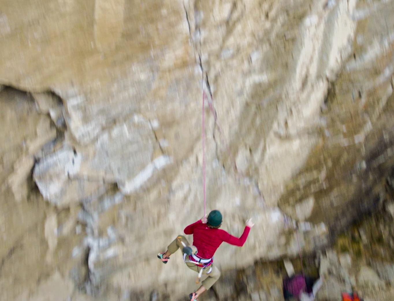 A rock climber in a Mammut red shirt falls while climbing a steep rock face, secured with Mammut climbing rope.