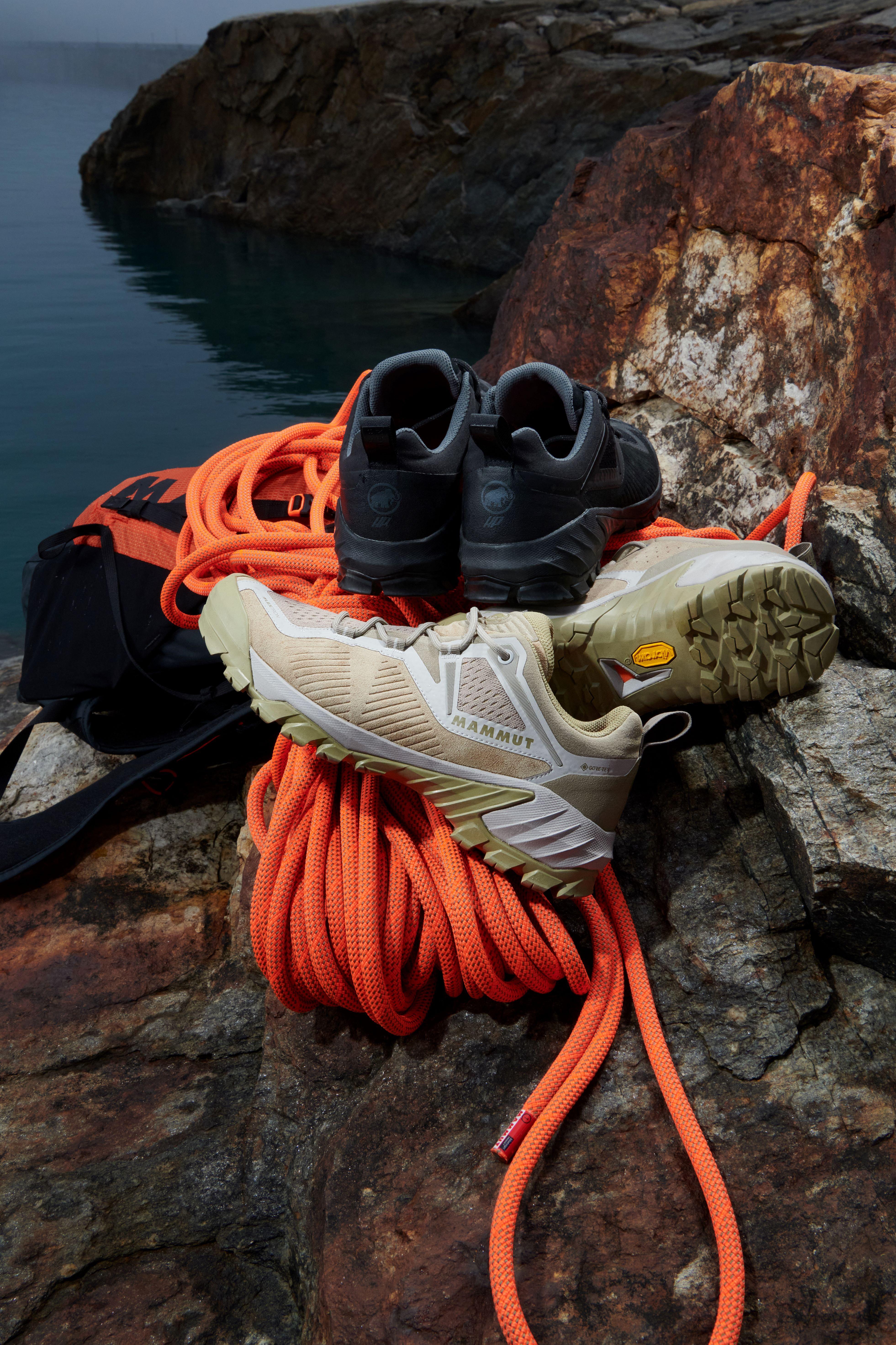 Mammut climbing shoes and rope on a rocky shore, overlooking a serene body of water.