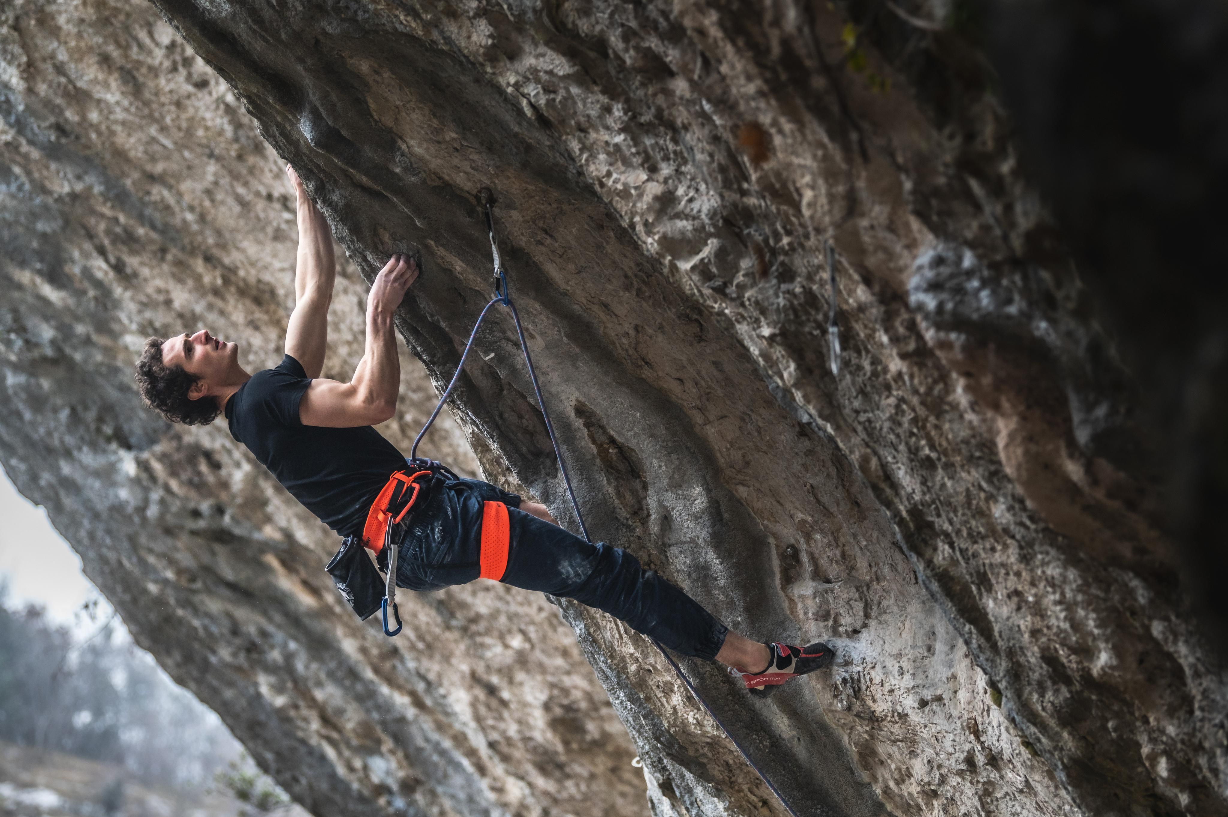 A climber wearing Mammut gear grips an overhanging rock face, ascending with Mammut ropes and harness in a stunning outdoor setting.