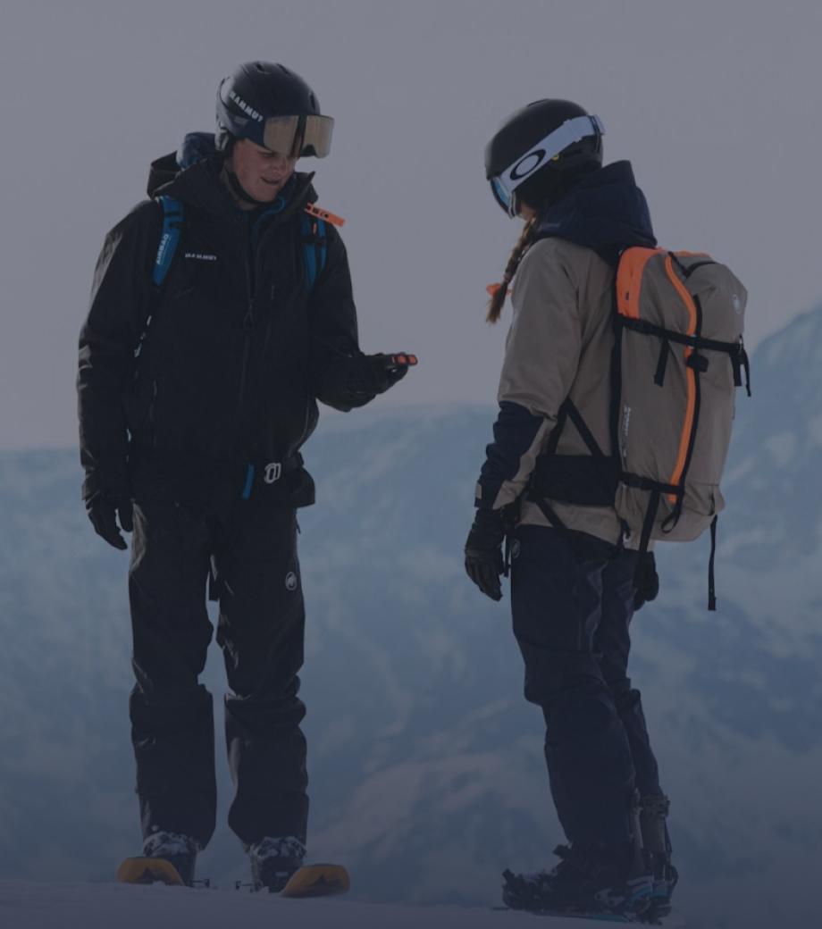 Two people in Mammut skiing gear stand on a snowy Alpine mountain slope, engaged in conversation.