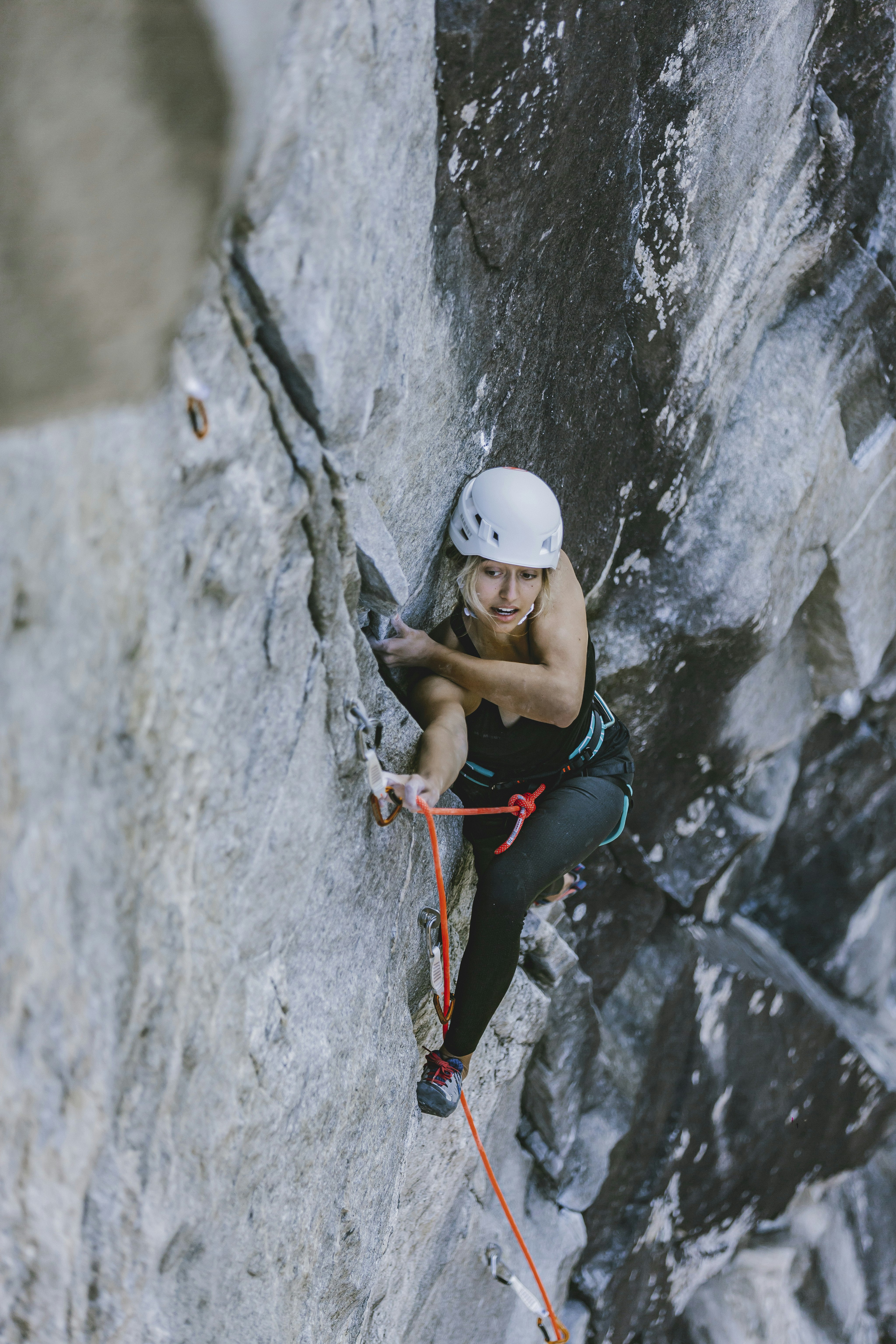 Woman climbing a high stone wall, secured with Mammut equipment.